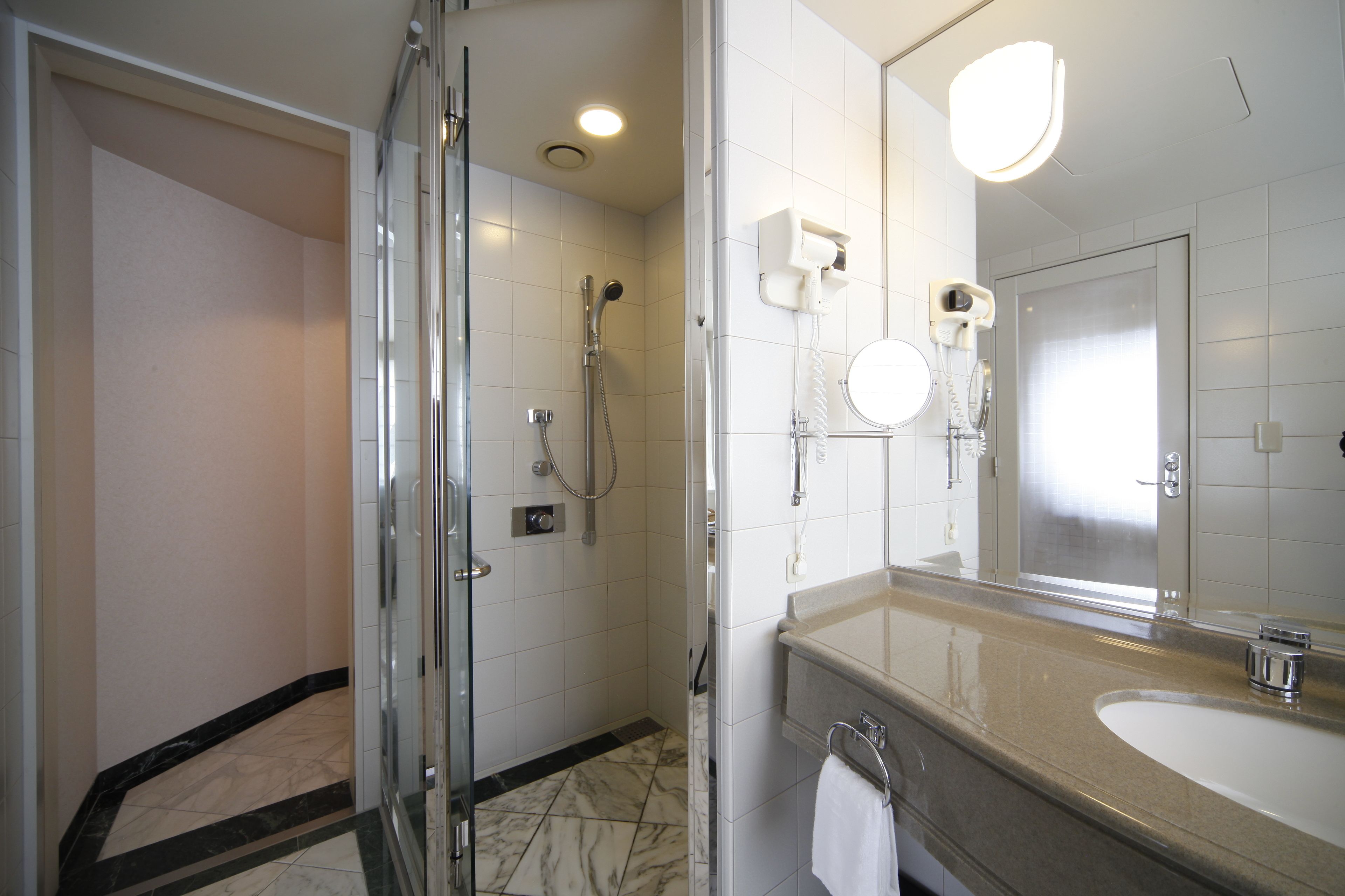 Un baño moderno con ducha de vidrio, un espejo grande y piso de baldosas de mármol.