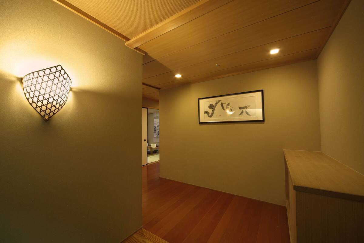 A hallway with a wooden floor, a wall-mounted light fixture, and a framed artwork.