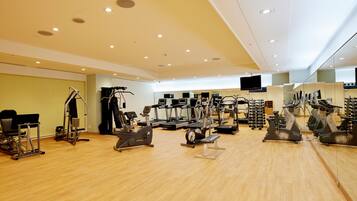 A spacious gym with various cardio and strength training equipment, a large mirror, and a television on the wall.