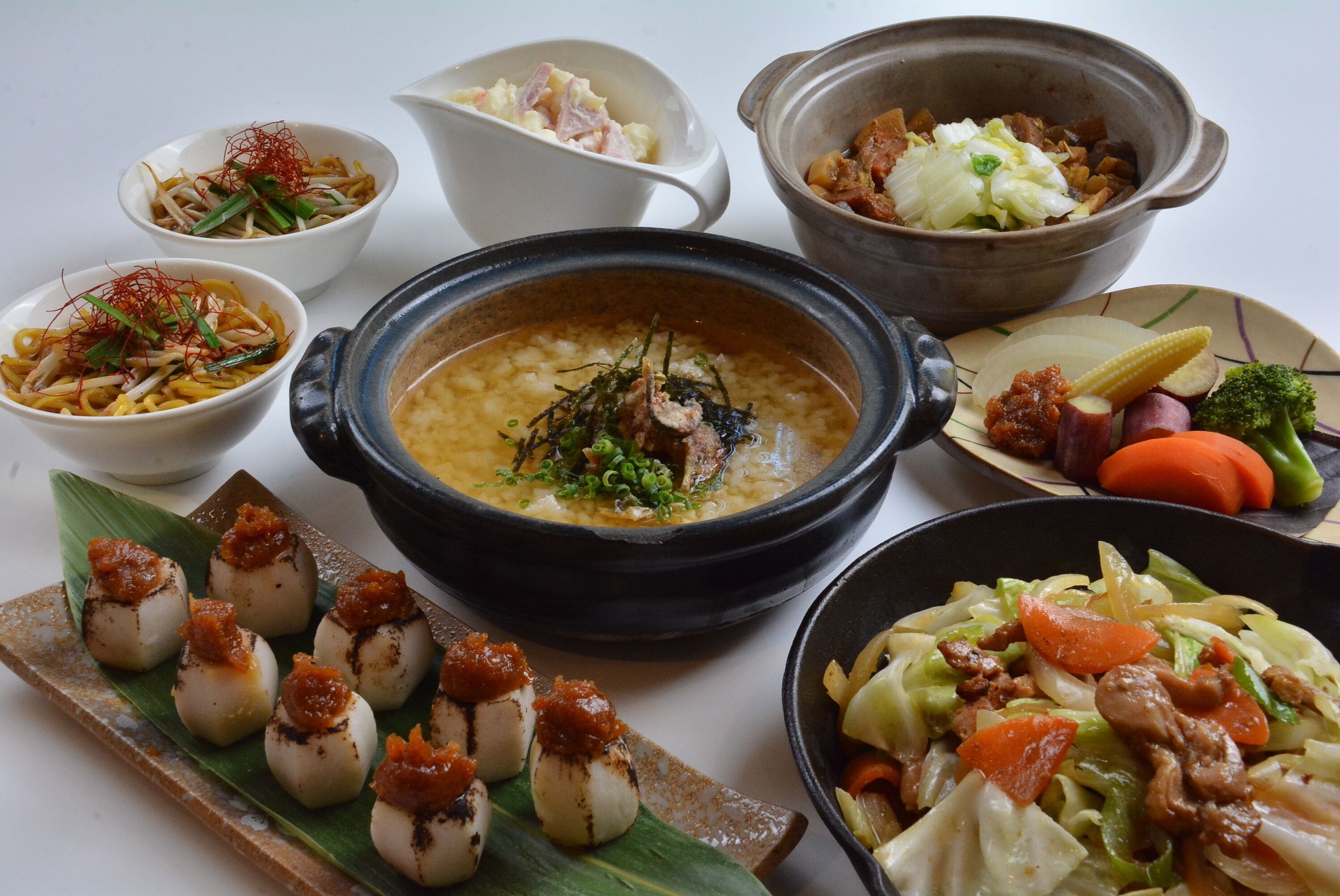 A variety of dishes including a large pot of soup, several small bowls of food, and a plate with dumplings.