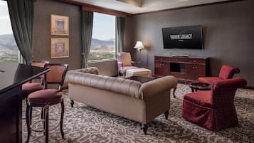Habitación de hotel con sofá, sillones, televisor y vistas a las montañas.