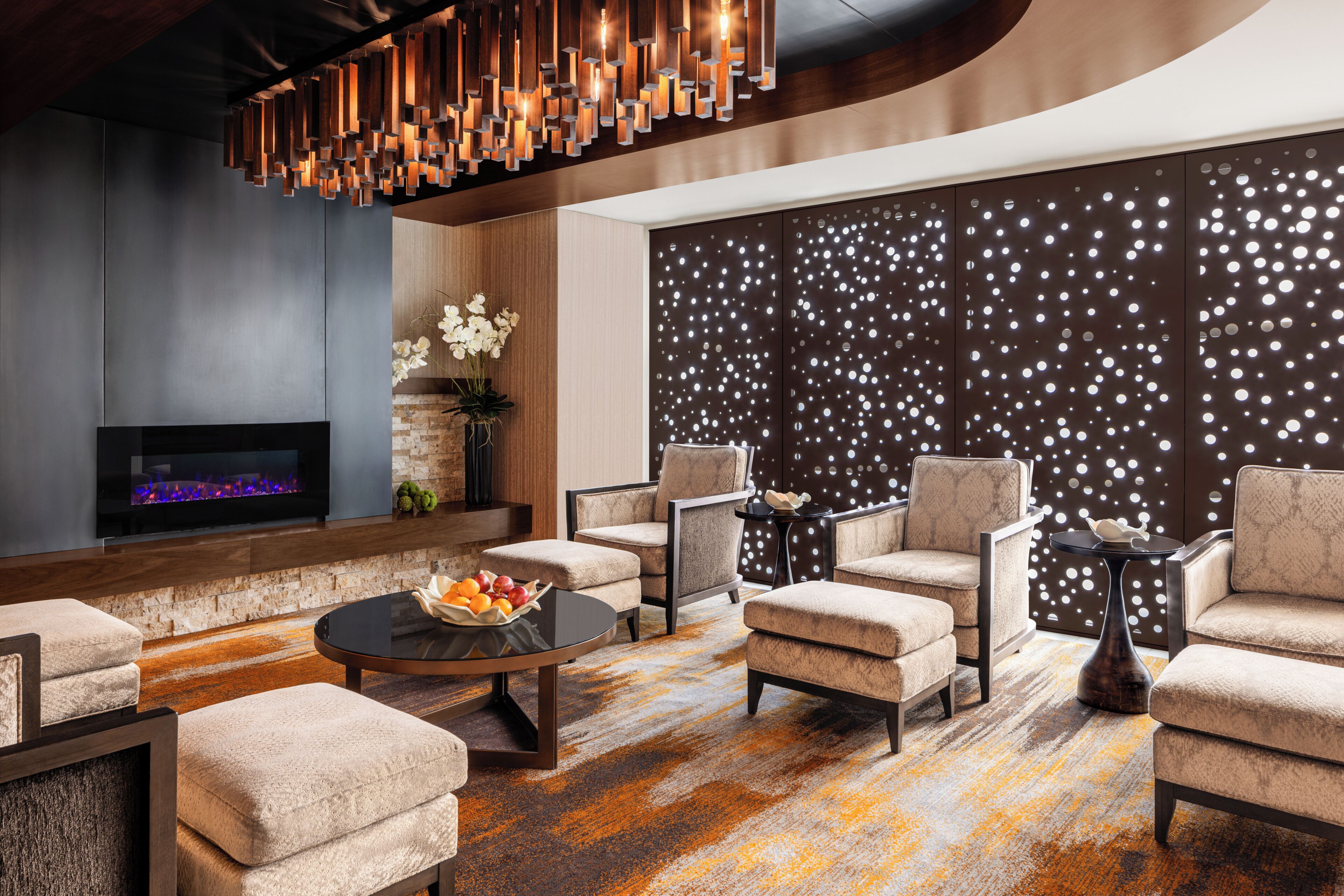Un espace de détente moderne doté d’une cheminée, de sièges confortables et d’un mur décoratif orné de motifs circulaires.