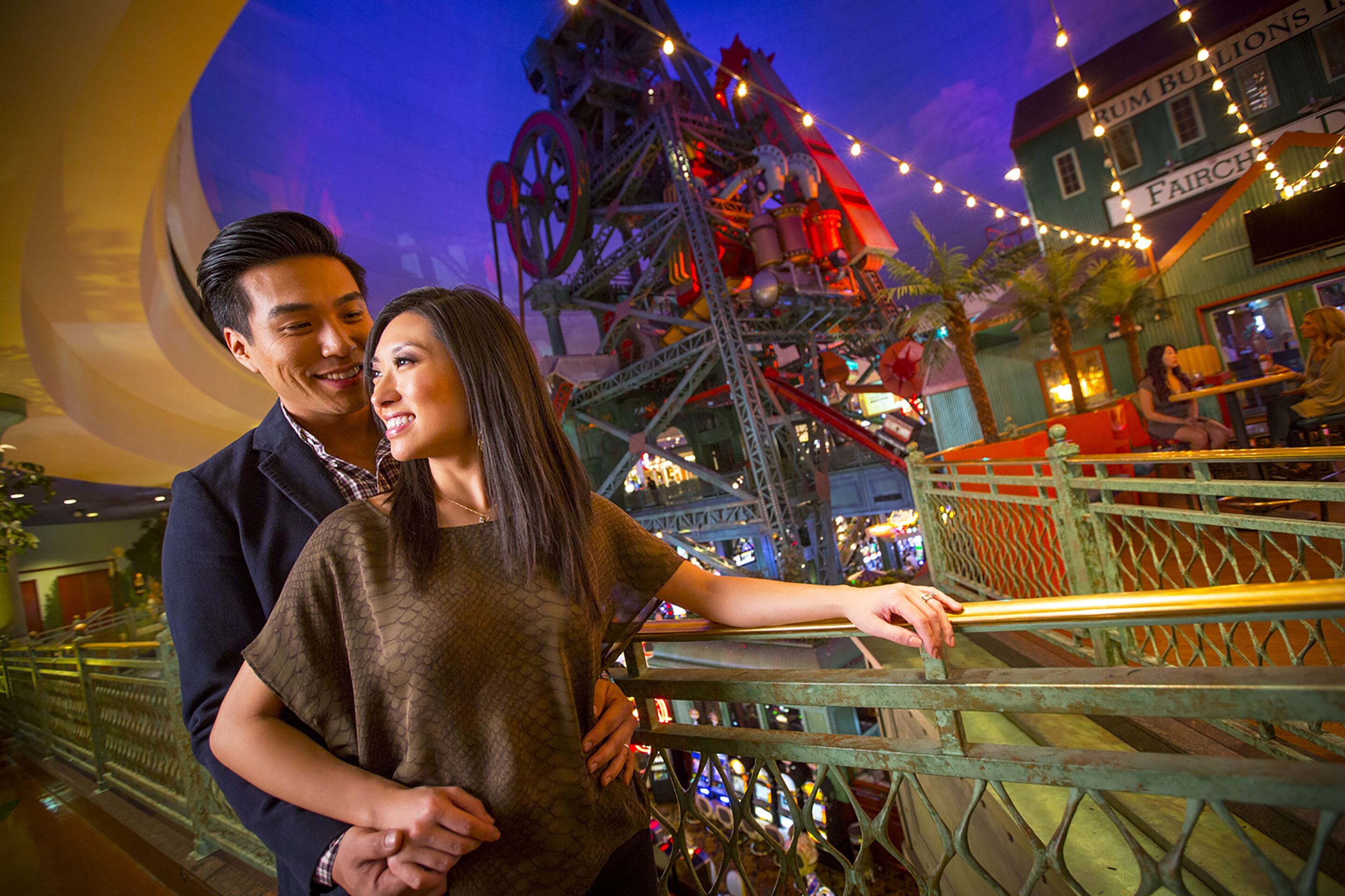 A couple standing on a balcony with a view of a Ferris wheel and a building labeled "Rum Bulls."