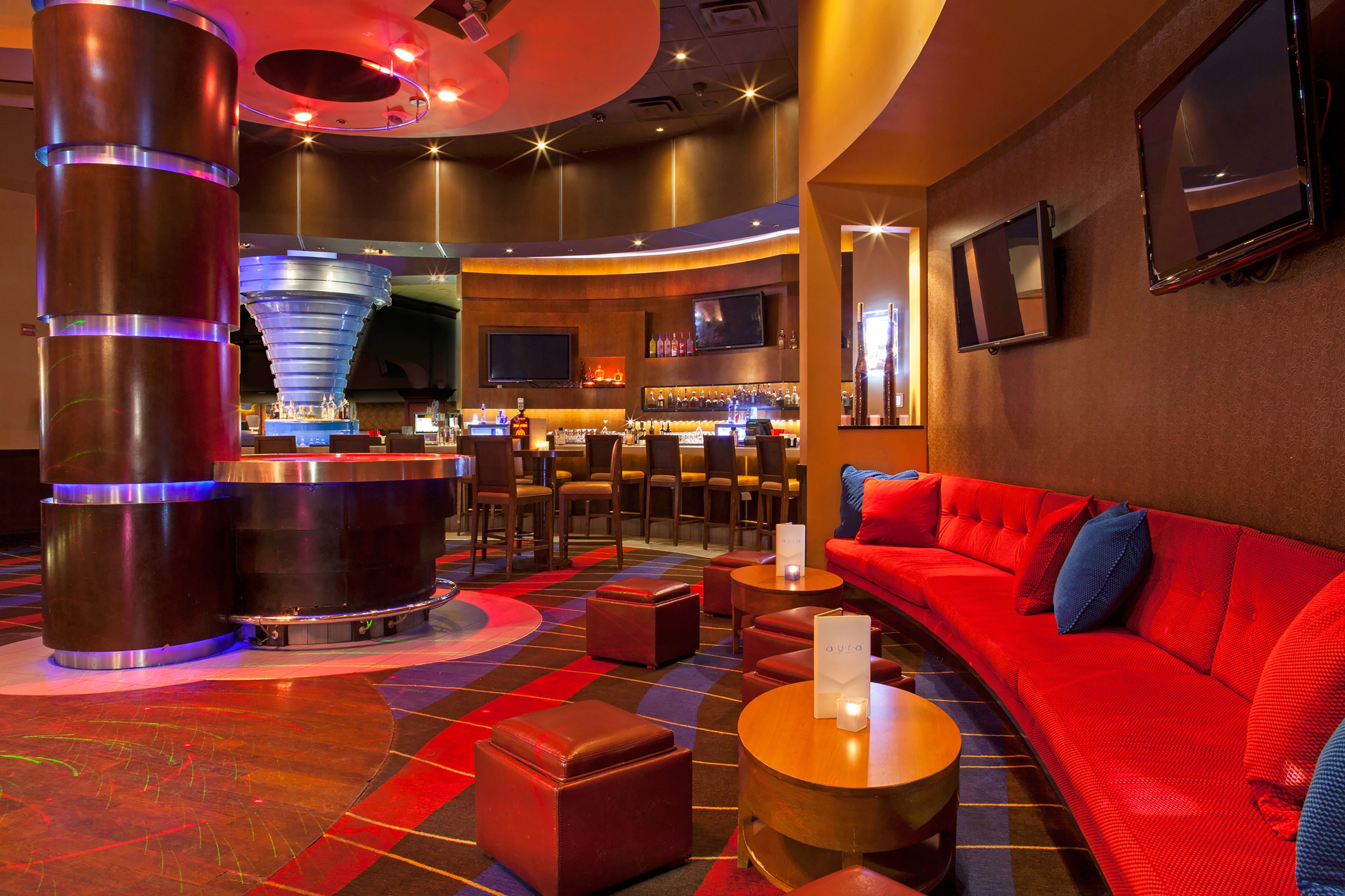 A modern bar area with a curved seating arrangement, a large cylindrical column, and a red sofa with blue cushions.