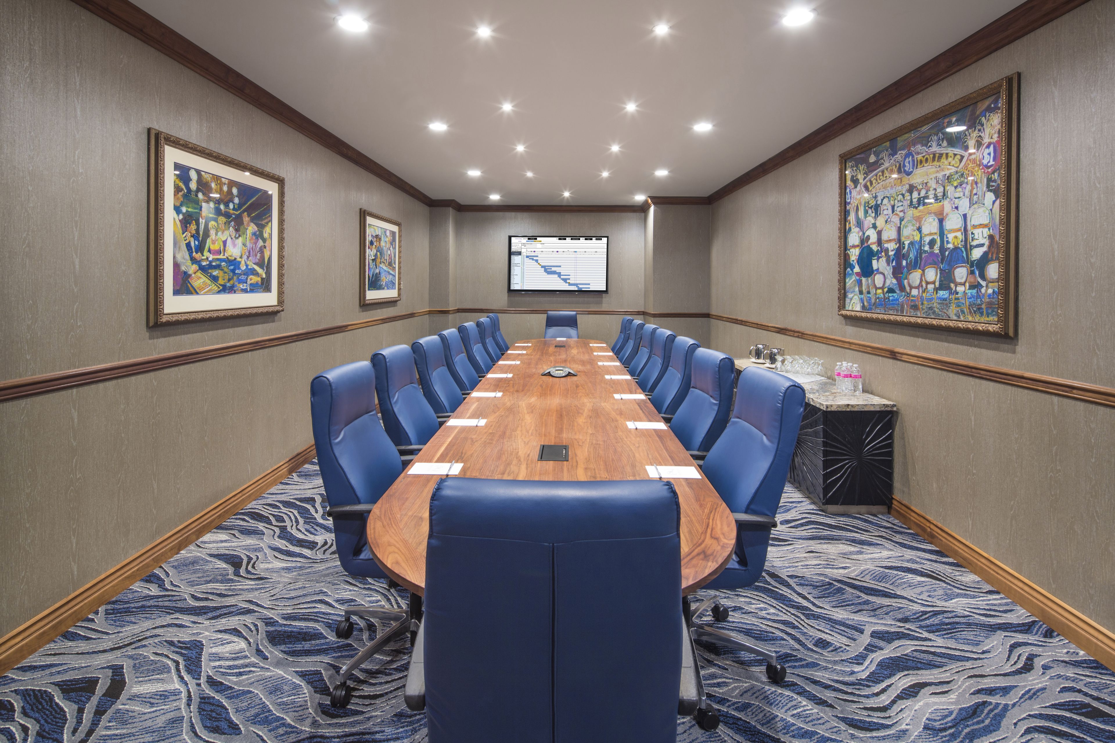 Une salle de conférence avec une longue table, des chaises bleues et un écran de projection.