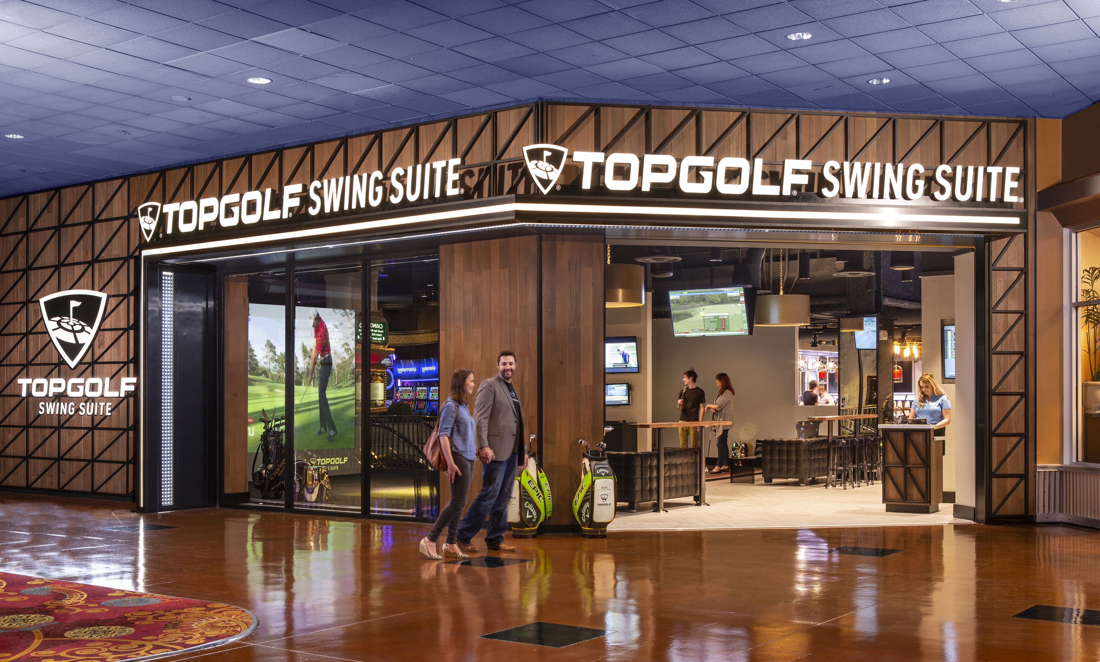 A TopGolf Swing Suite entrance with a wooden facade, large screens, and a reception area.