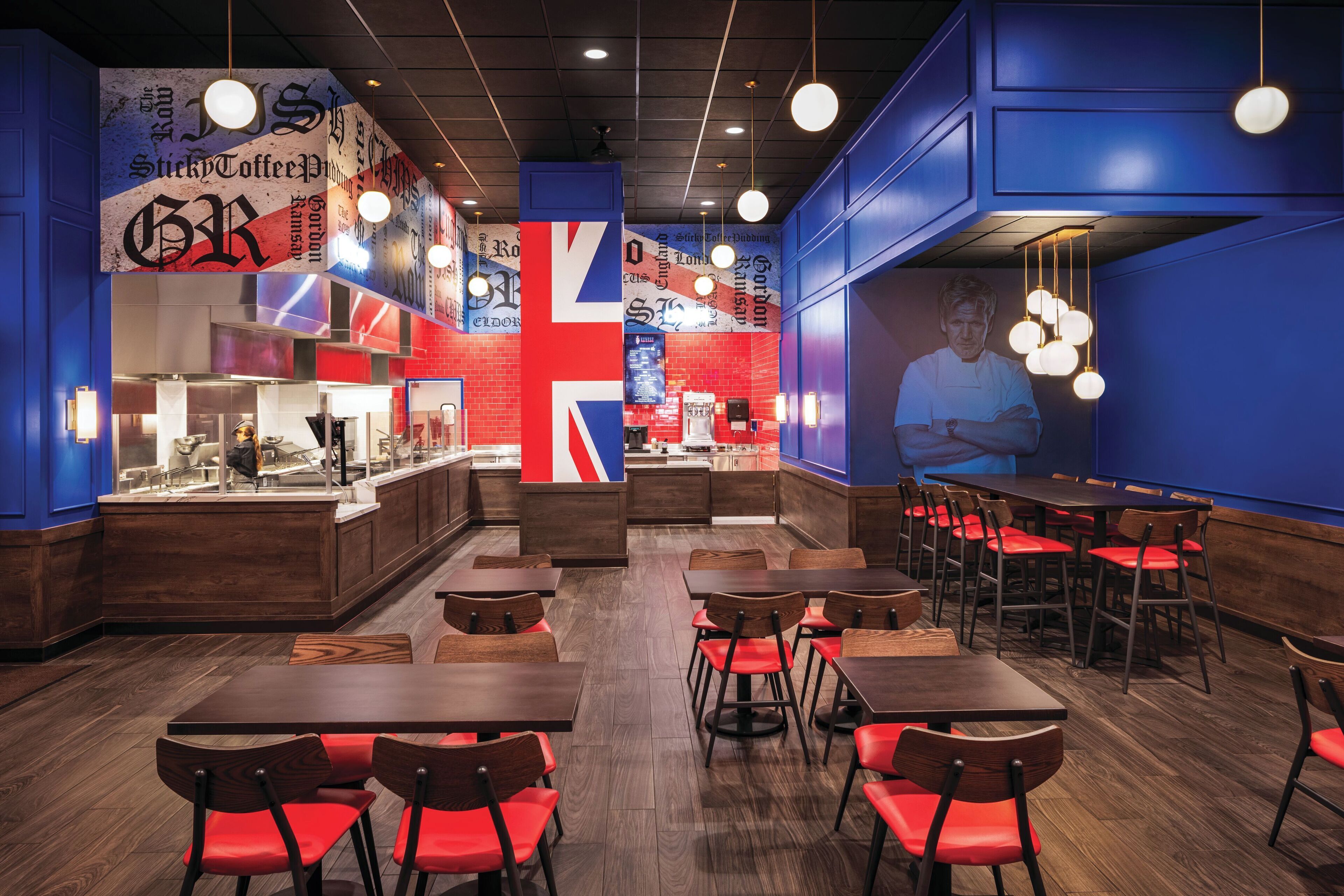 Ein Restaurant mit Holztischen und roten Stühlen, einer Theke mit Speisekarte und einer großen Union Jack-Flagge an der Wand.