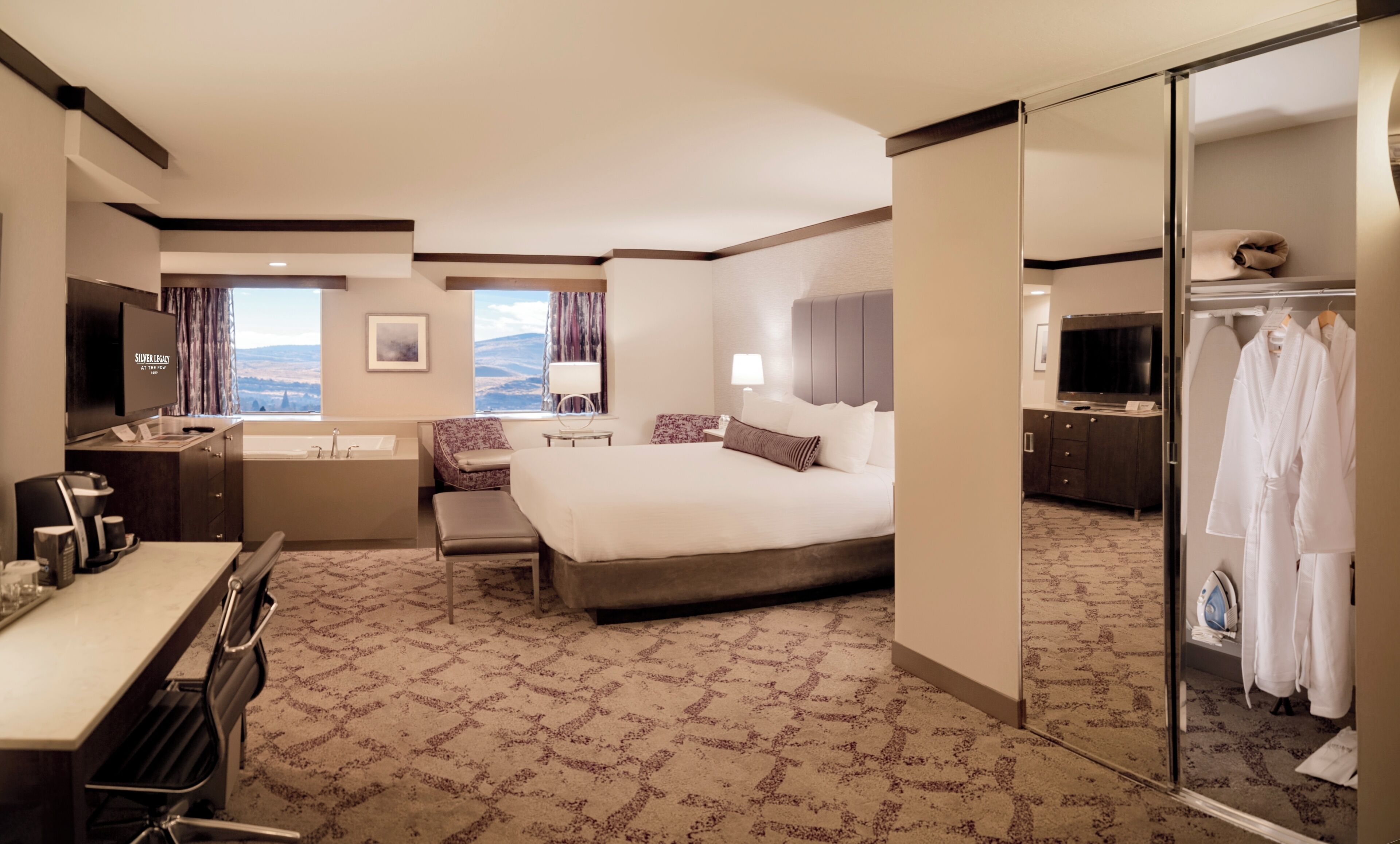 Ein Hotelzimmer mit einem großen Bett, einem Schreibtisch mit Stuhl, einem Schminktisch mit Spiegel, einem Fernseher und Blick auf die Berge.