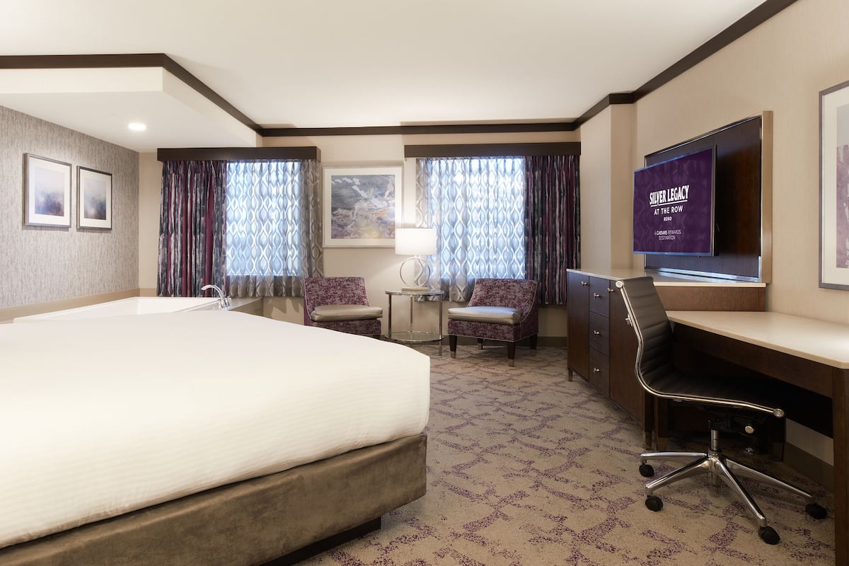 A hotel room with a large bed, a desk, a chair, a TV, and a window with curtains.