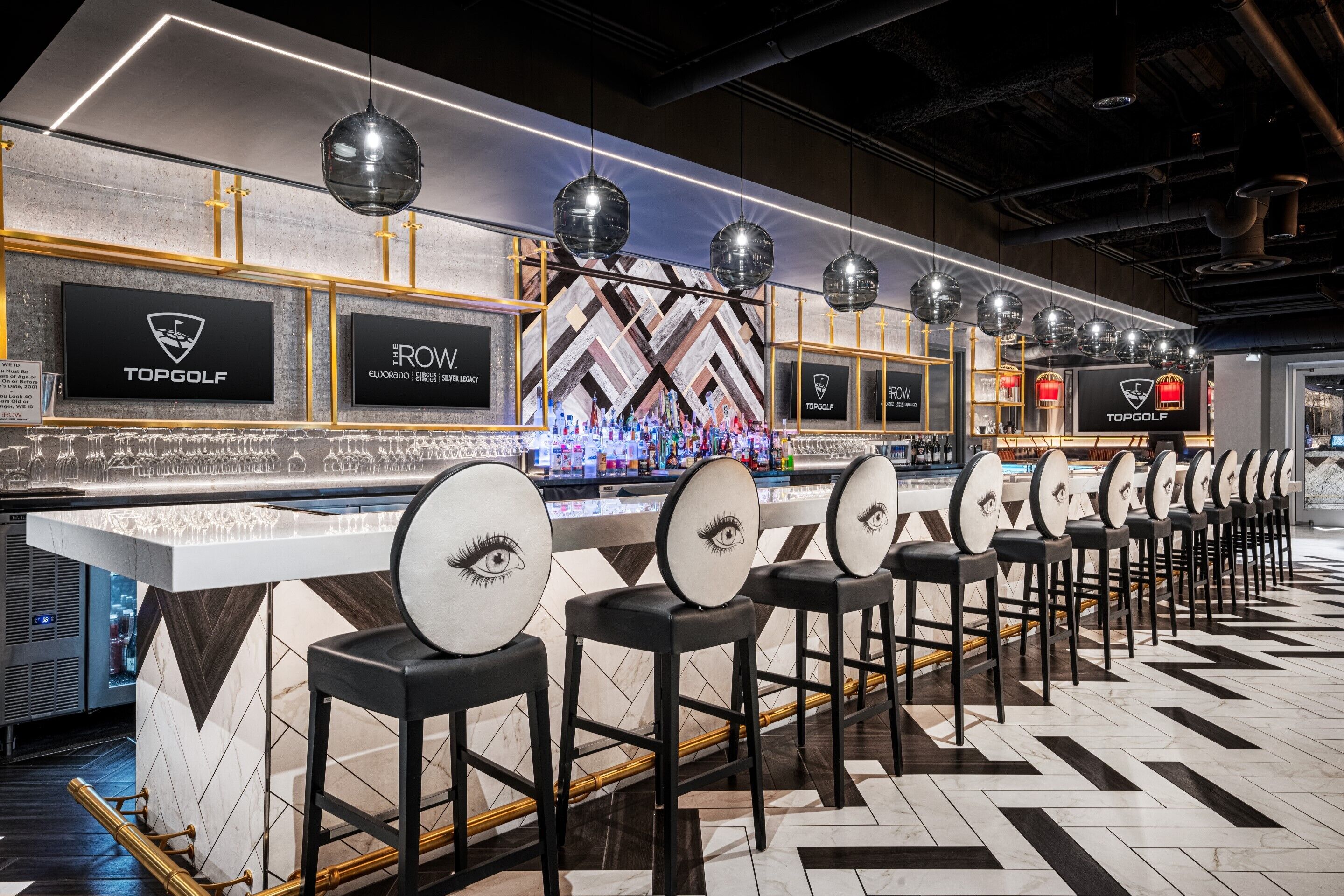 A bar area with multiple stools, a counter with a logo, and pendant lighting.