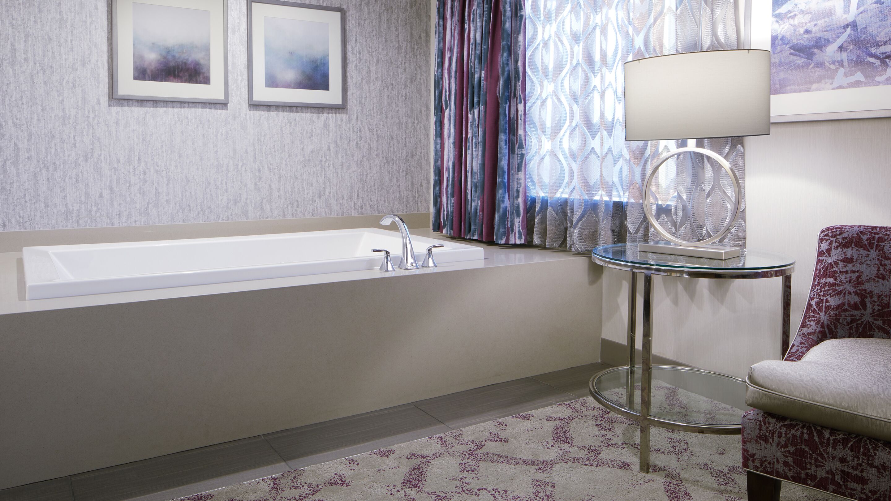 A modern bathroom with a bathtub, a round glass table, and a patterned chair.