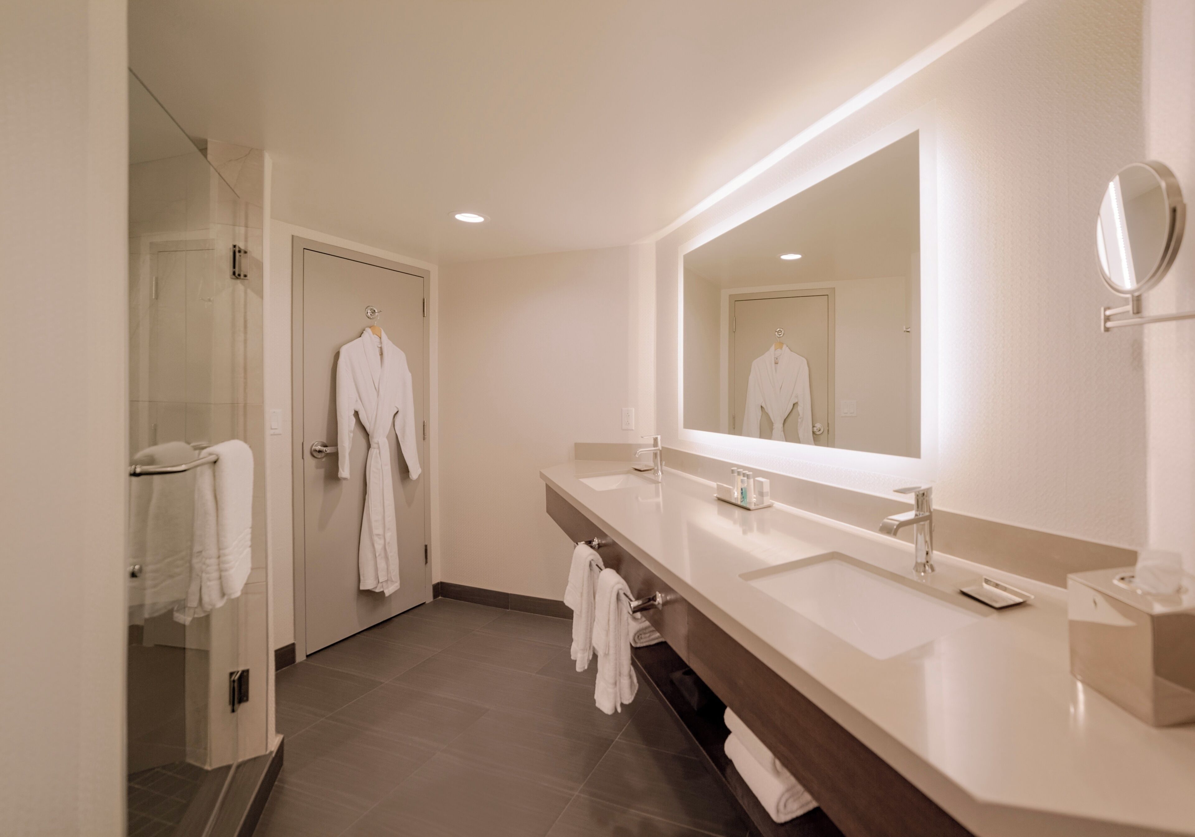 A modern bathroom with a large mirror, two sinks, and a glass shower enclosure.