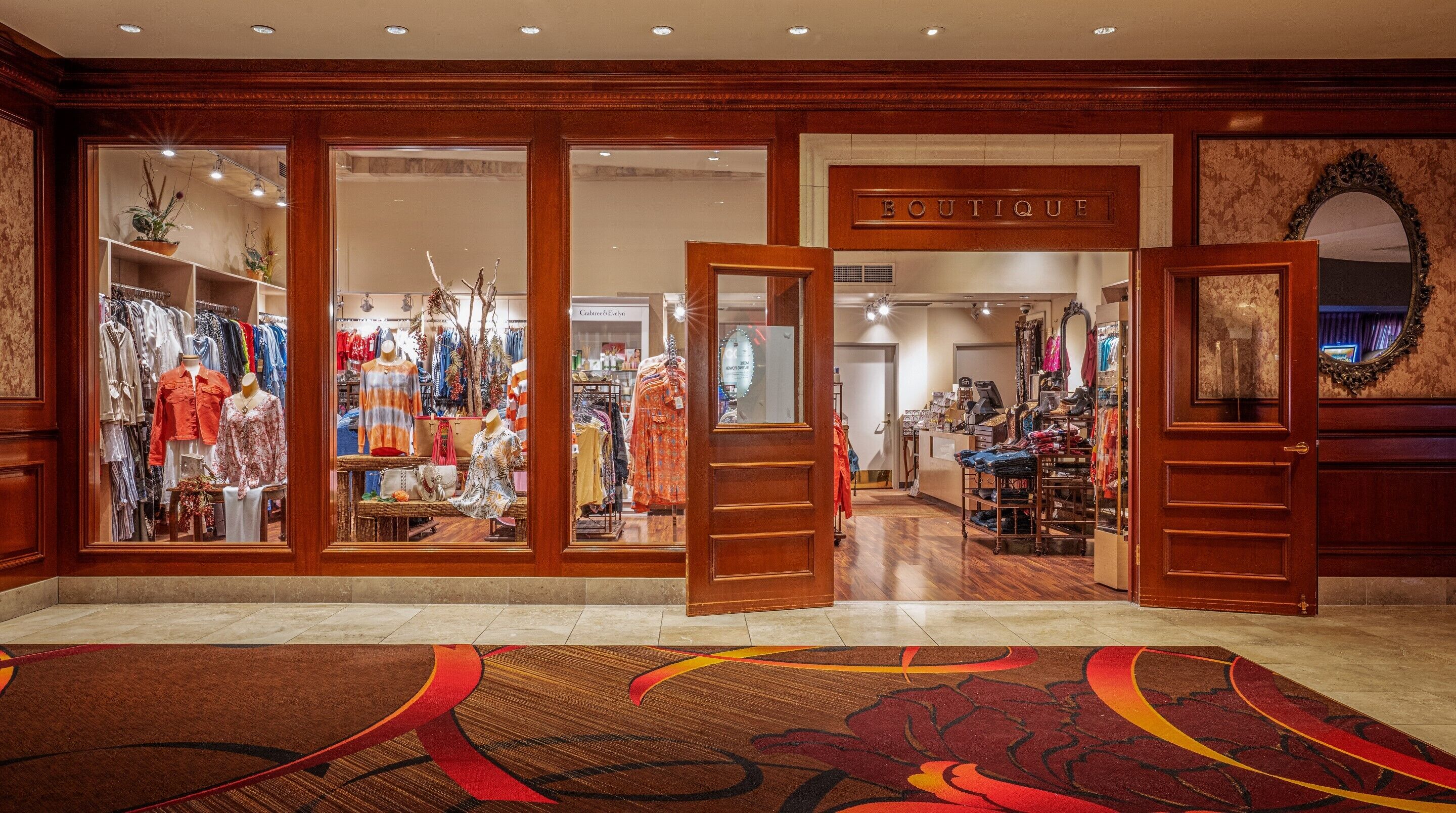 A boutique with wooden doors, a variety of clothing on display, and a carpeted floor.