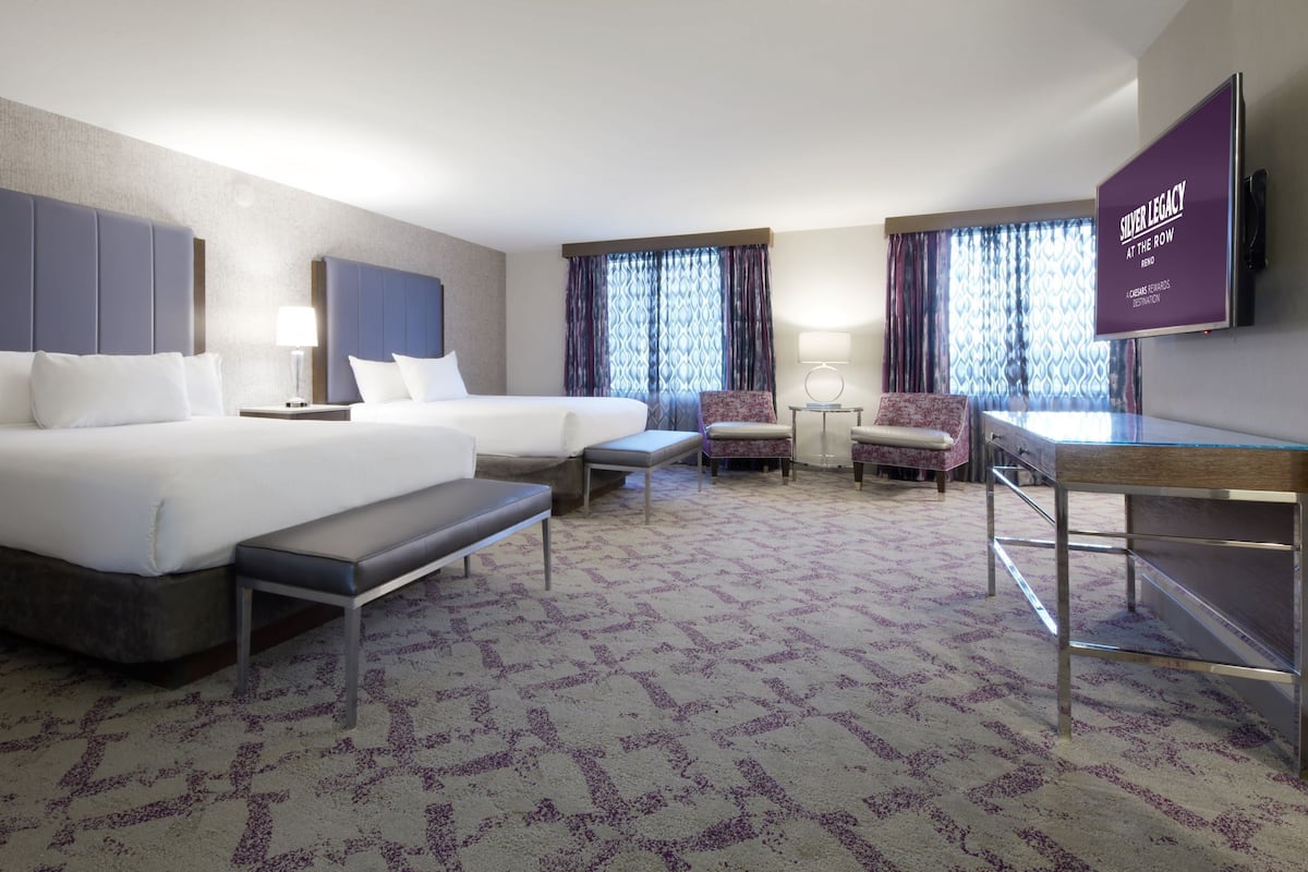 A hotel room with two beds, a desk, a chair, and a television.