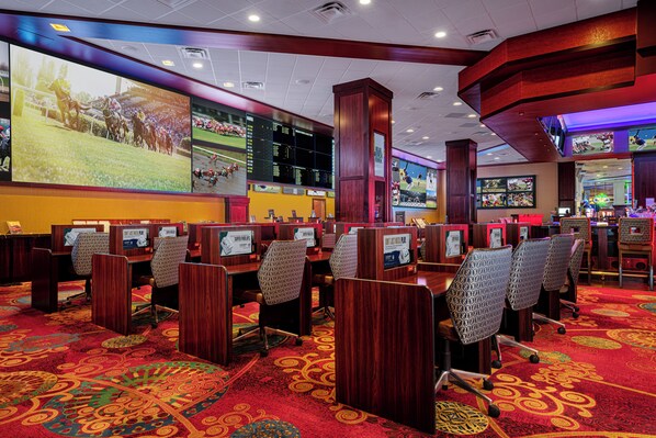 A casino with multiple gaming tables and a large screen displaying a horse race. - Silver Legacy Reno- A Caesars Rewards Destination (Reno)