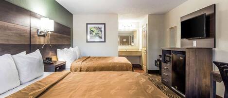 A hotel room with two beds, a desk, a television, a microwave, and a bathroom visible in the background.