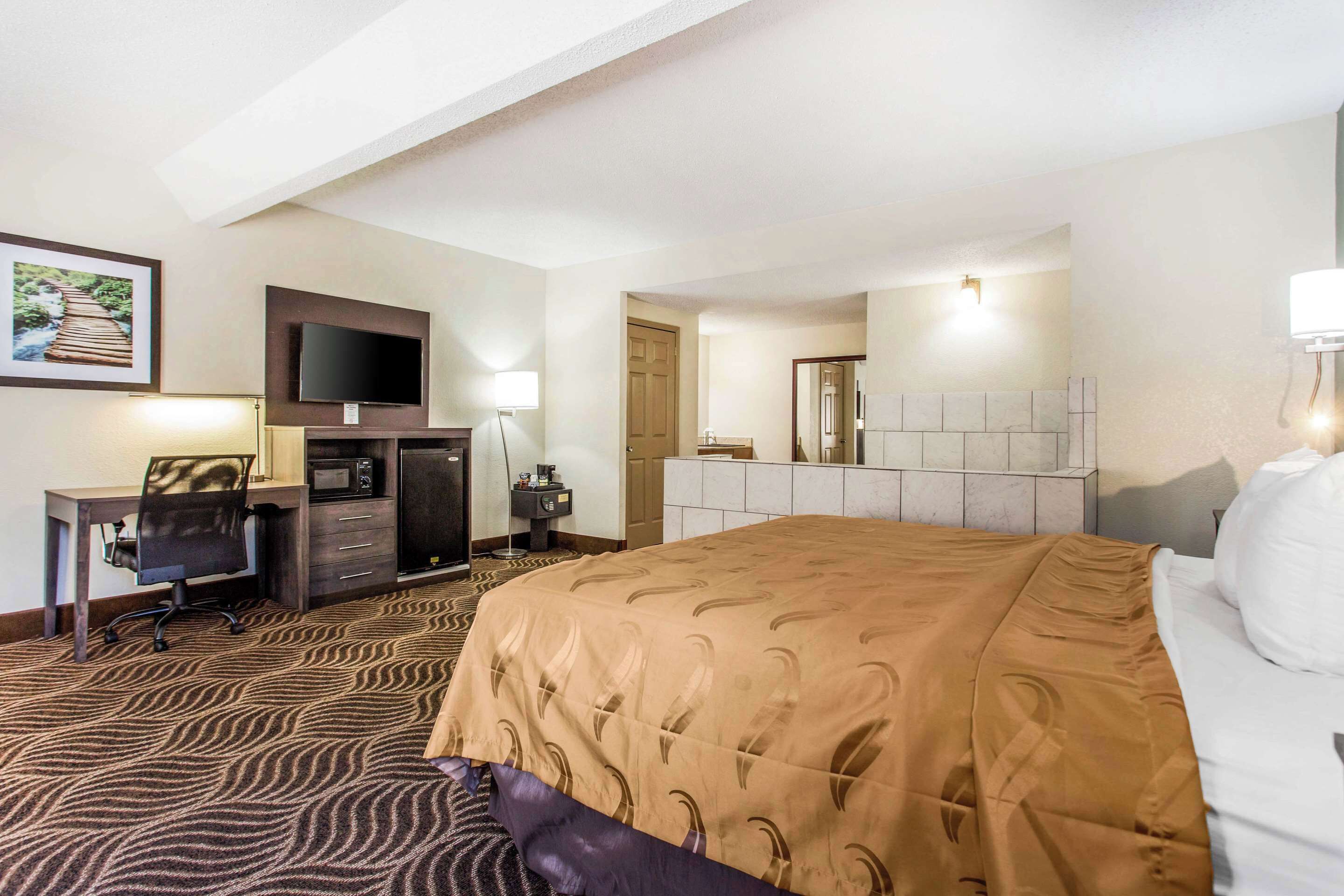 A hotel room with a bed, desk, chair, television, and a bathroom visible through an open door.