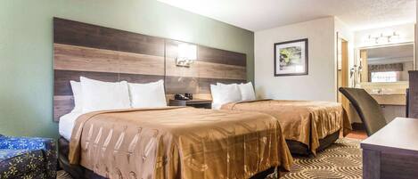 A hotel room with two beds, a desk, a chair, a mirror, and a patterned carpet.
