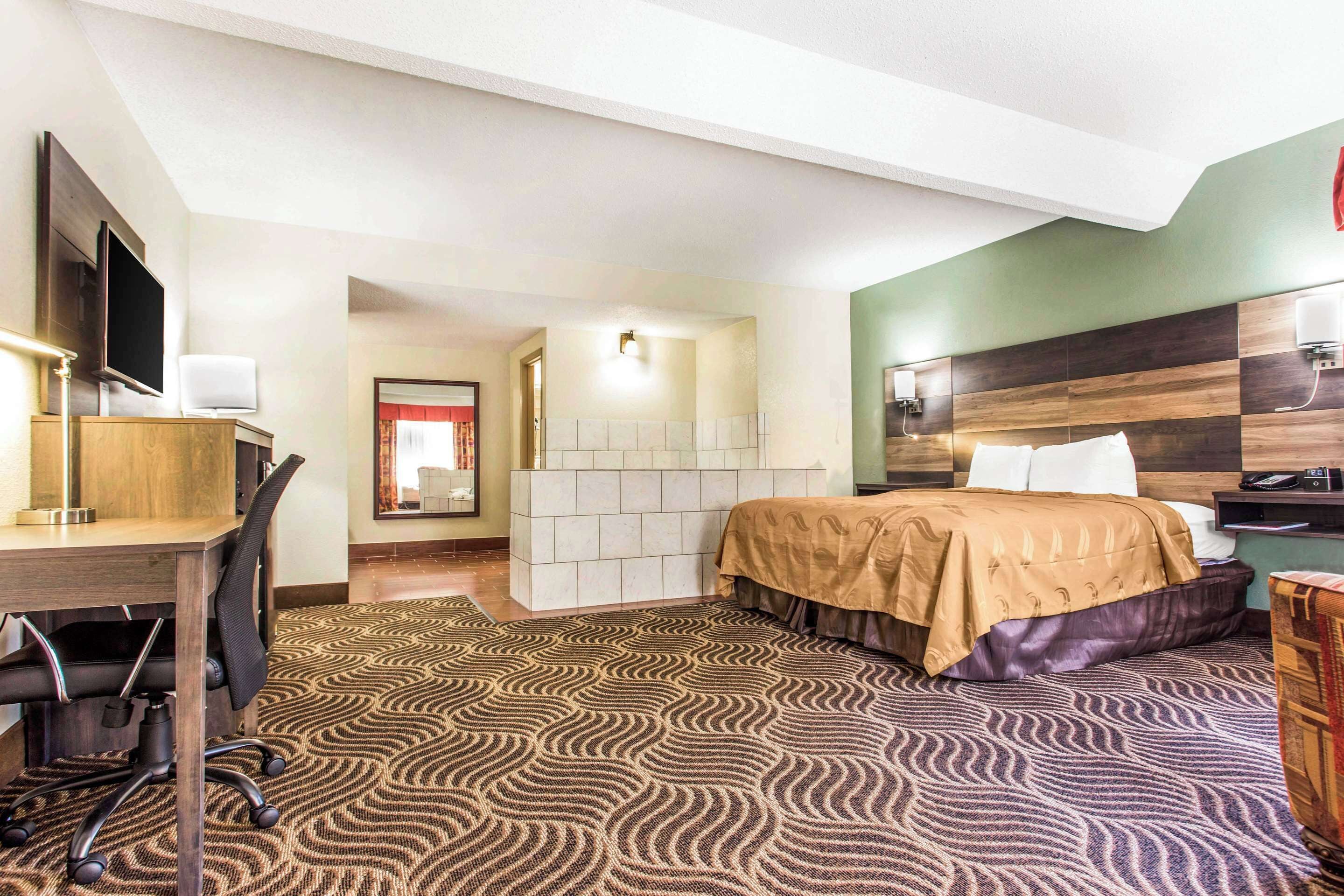 A hotel room with a bed, desk, chair, and a television.