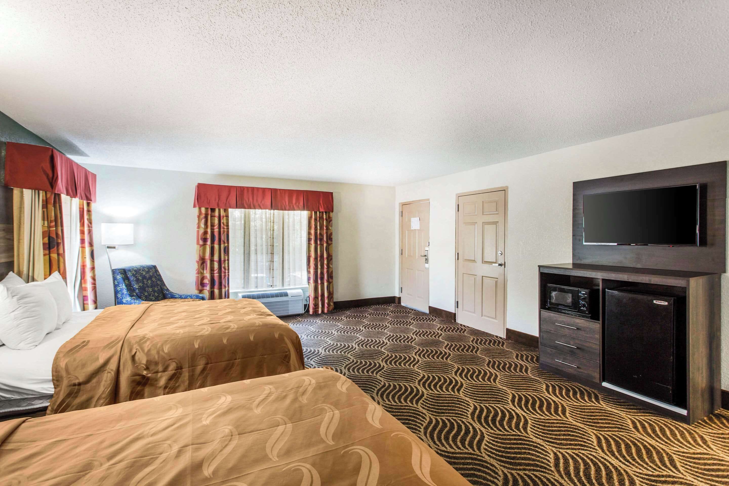 A hotel room with two beds, a television, a minibar, and a patterned carpet.