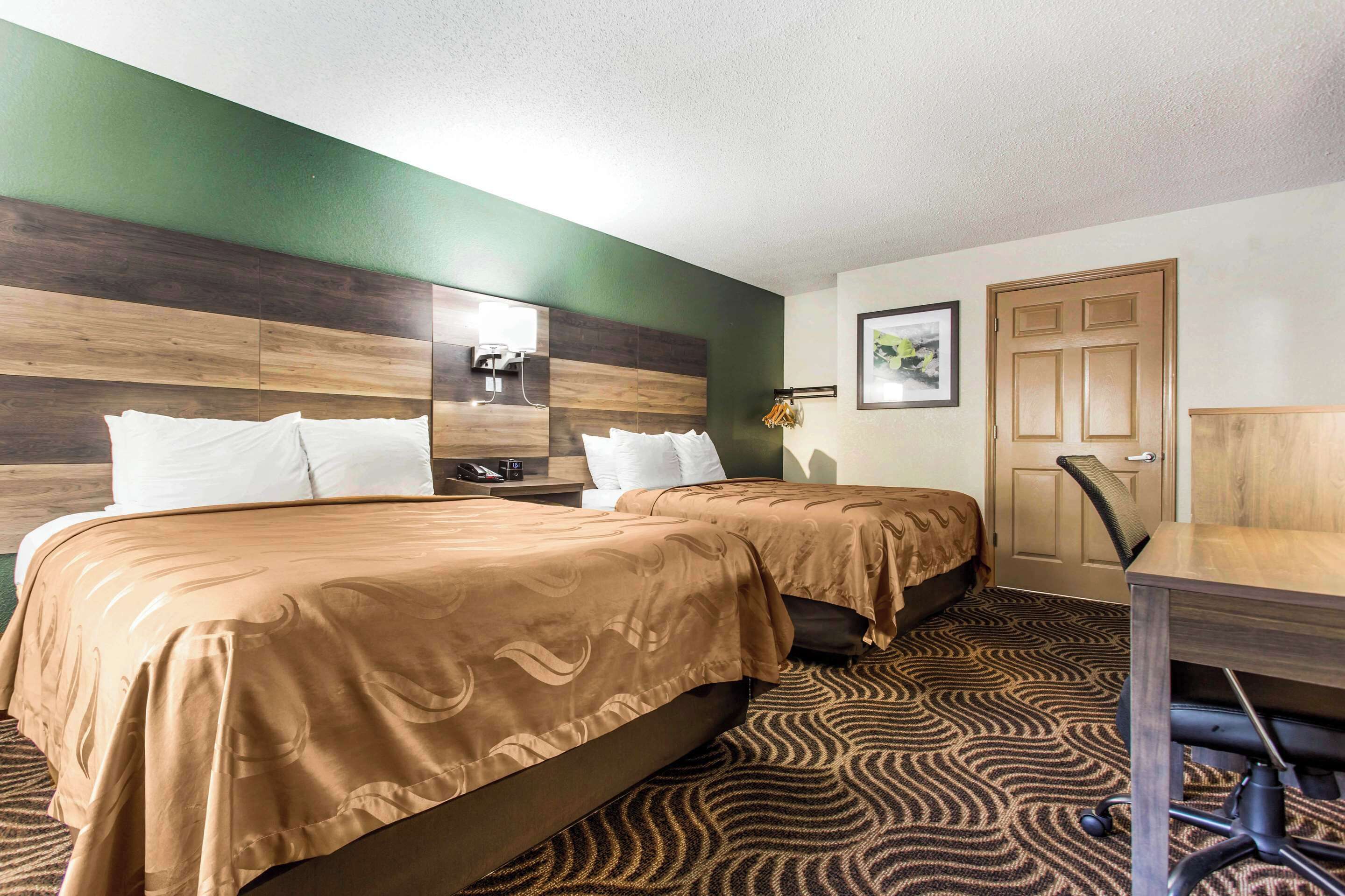 A hotel room with two beds, a desk, a chair, a mirror, and a door.