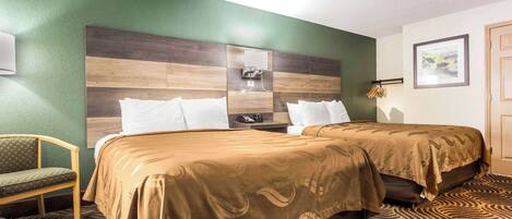 A hotel room with two beds, a green wall, a wooden headboard, a green chair, and a patterned carpet.