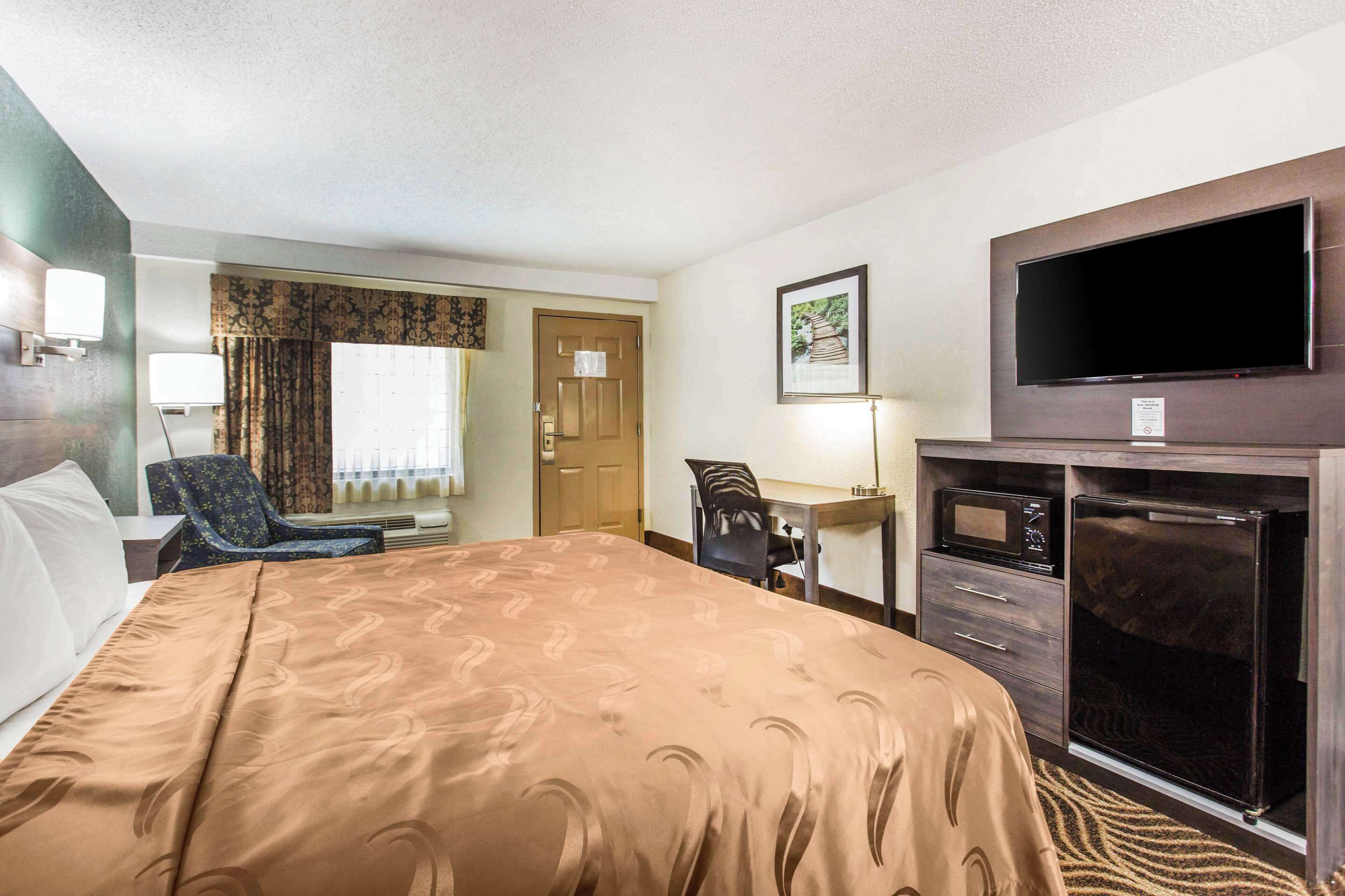 A hotel room with a large bed, a desk, a chair, a television, and a microwave.