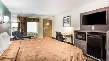 Een hotelkamer met een groot bed, een bureau, een stoel, een televisie en een magnetron.
