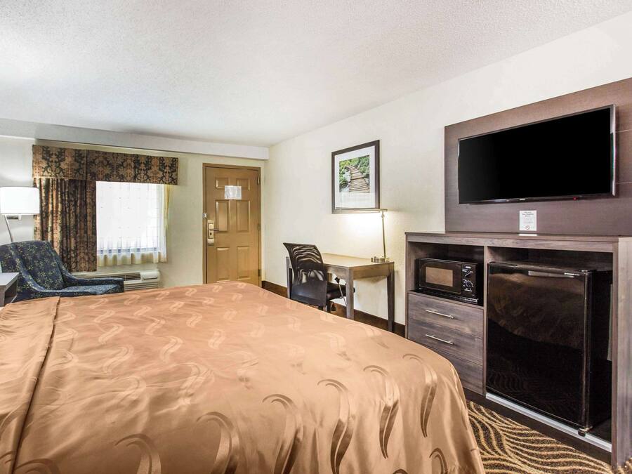 Une chambre d’hôtel avec un grand lit, un bureau, une chaise, une télévision et un four à micro-ondes.