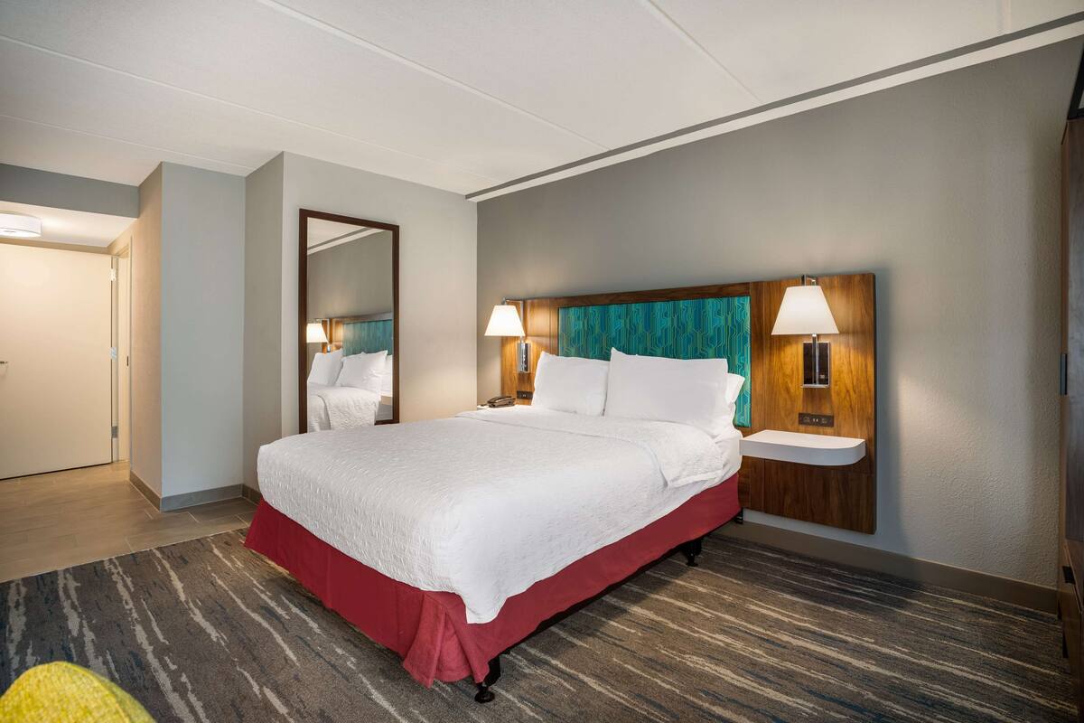 A hotel room with a large bed, two bedside tables with lamps, a mirror, and a red skirted bed base.
