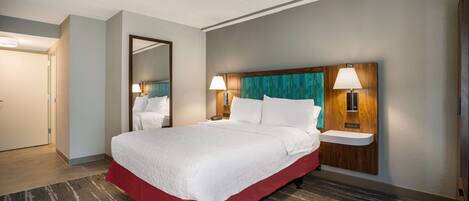 A hotel room with a large bed, two bedside tables with lamps, a mirror, and a red skirted bed base.