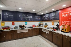 A bakery counter with various baking tools and ingredients, a chalkboard with food illustrations, and a red sign promoting waffles.
