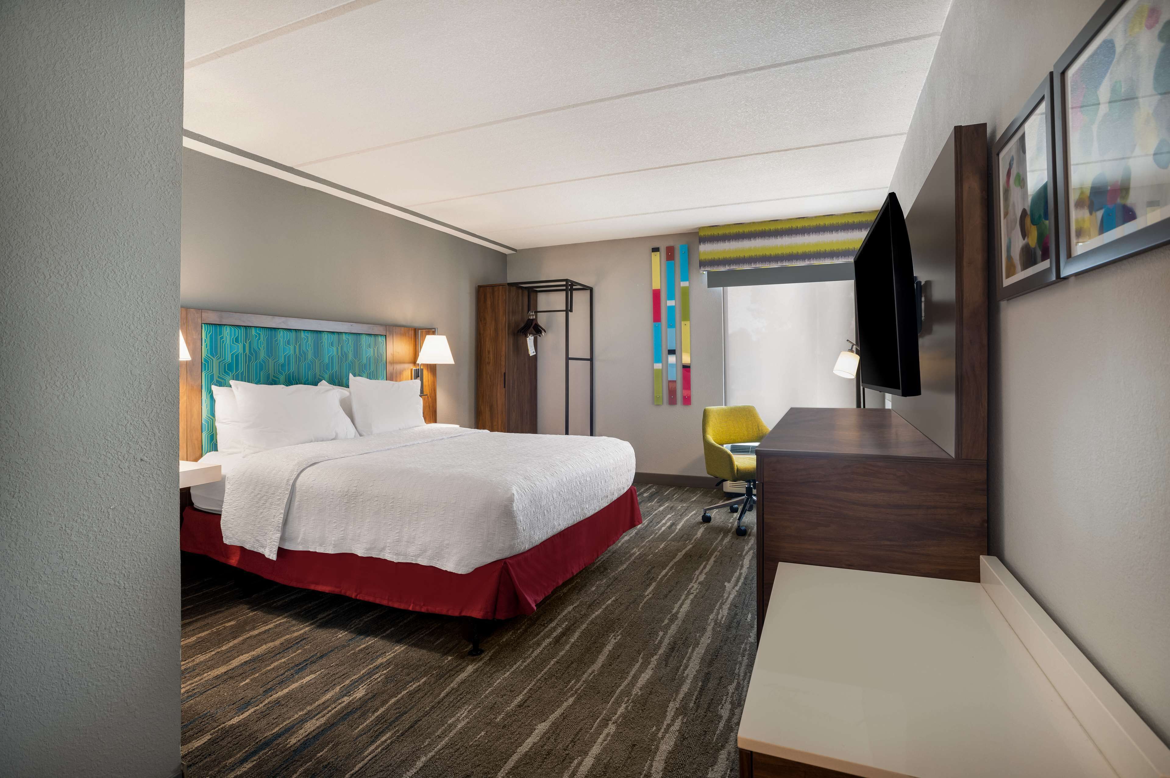 A hotel room with a bed, desk, chair, and a television.