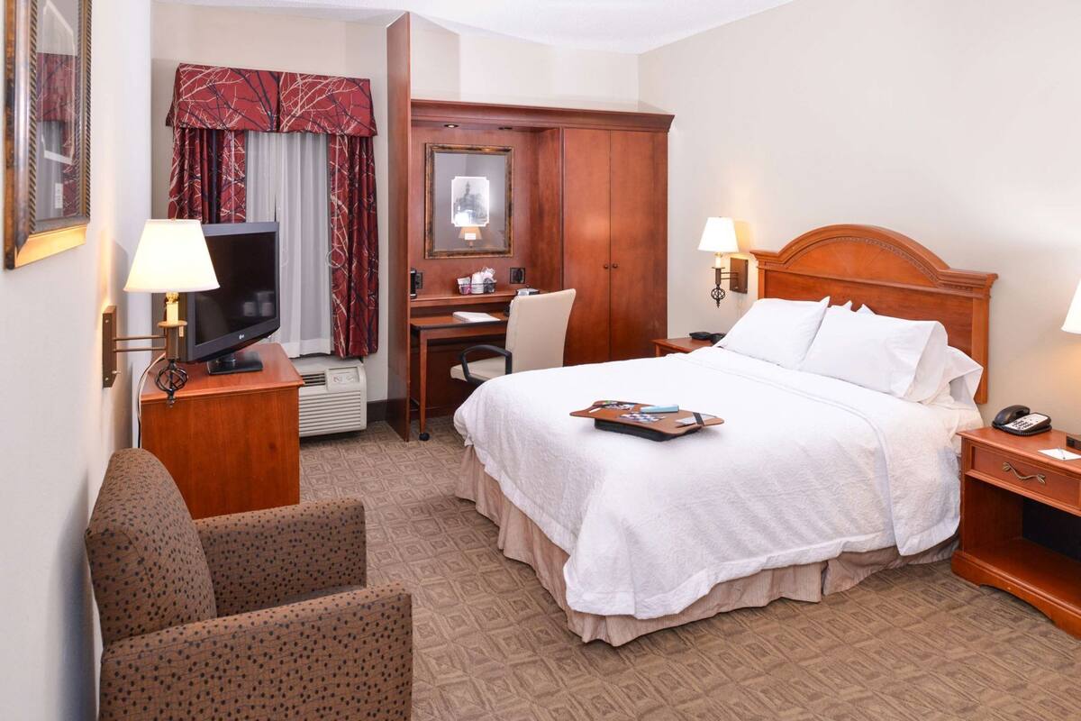 A hotel room with a bed, desk, chair, and a TV.