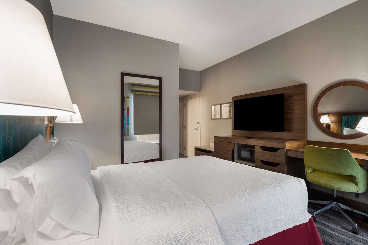 A hotel room with a bed, a desk with a television, a chair, and a mirror.
