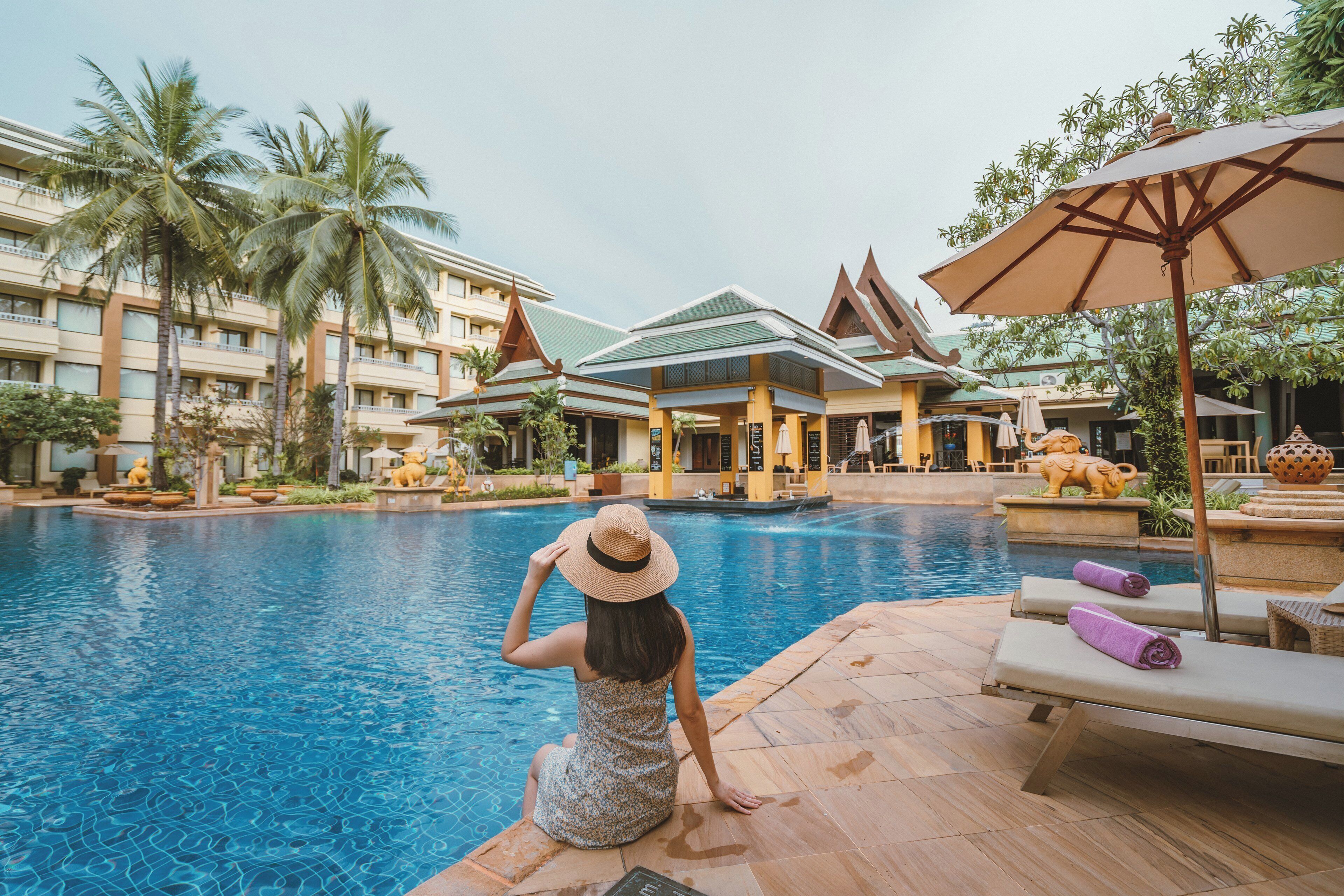 A poolside area with a view of a hotel building, palm trees, and a statue.