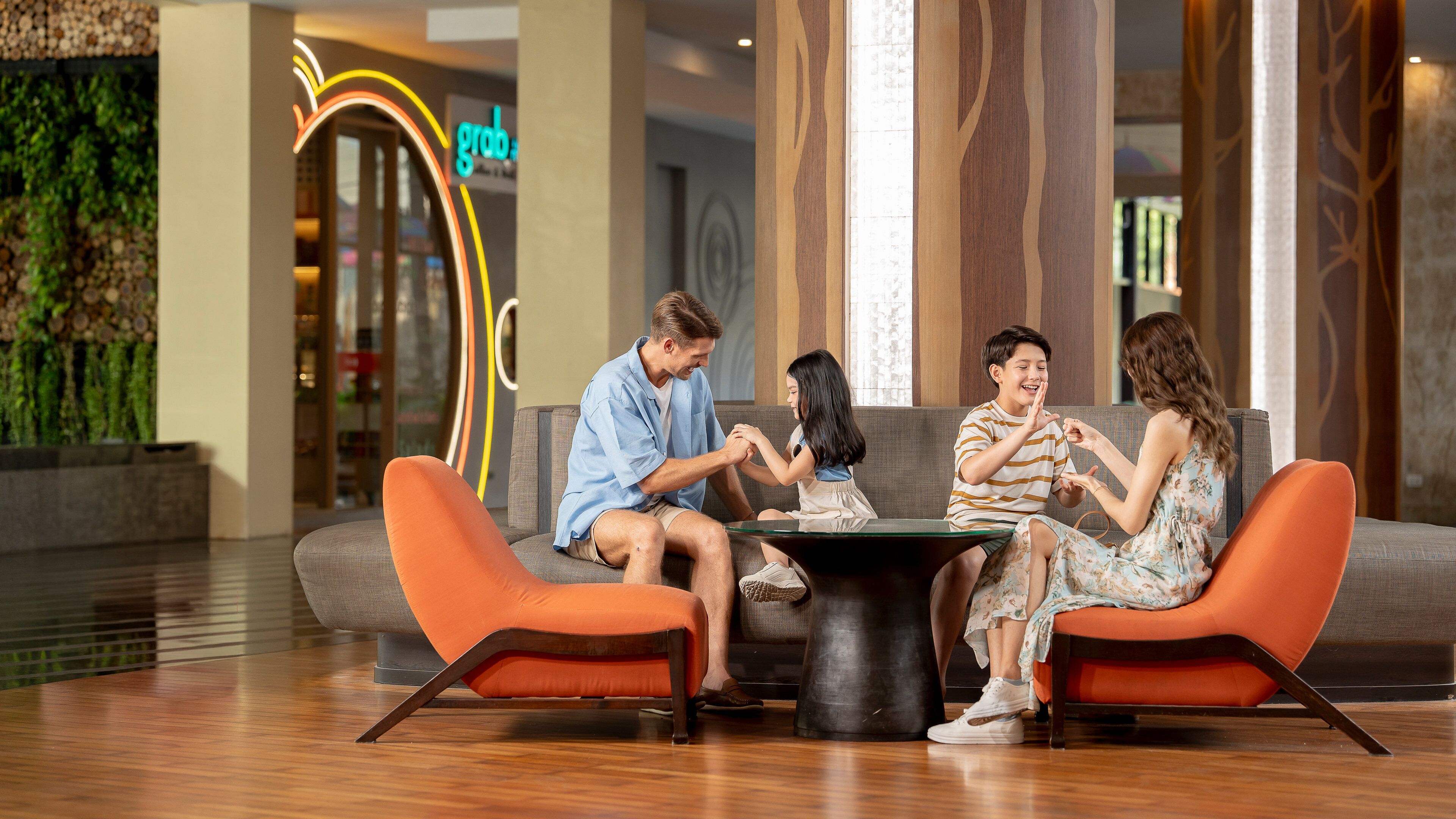 Een gezin zit op een moderne bank met oranje kussens in een goed verlichte lobby, met een zichtbaar 'grobo'-bord op de achtergrond.