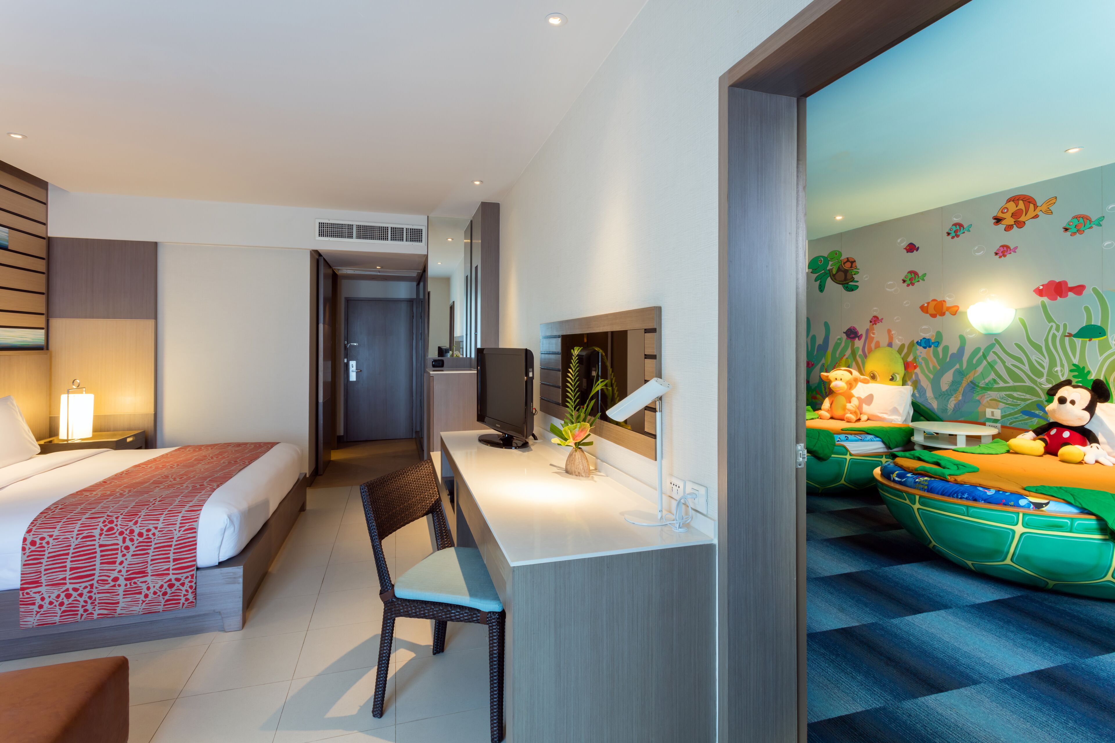 Ein Hotelzimmer mit Bett, Schreibtisch, Stuhl und Wandgemälde mit Unterwasser-Motiv.