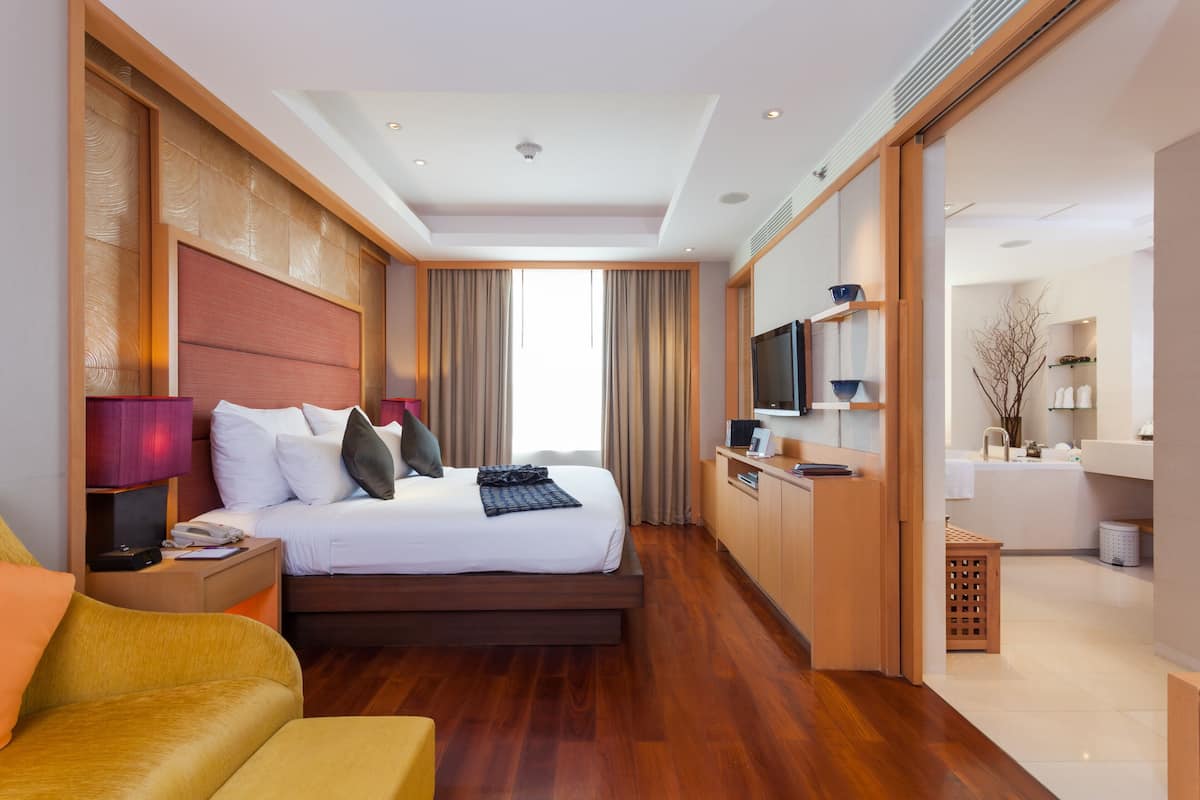 A modern hotel room with a large bed, a desk, a television, and a bathroom visible through an open door.