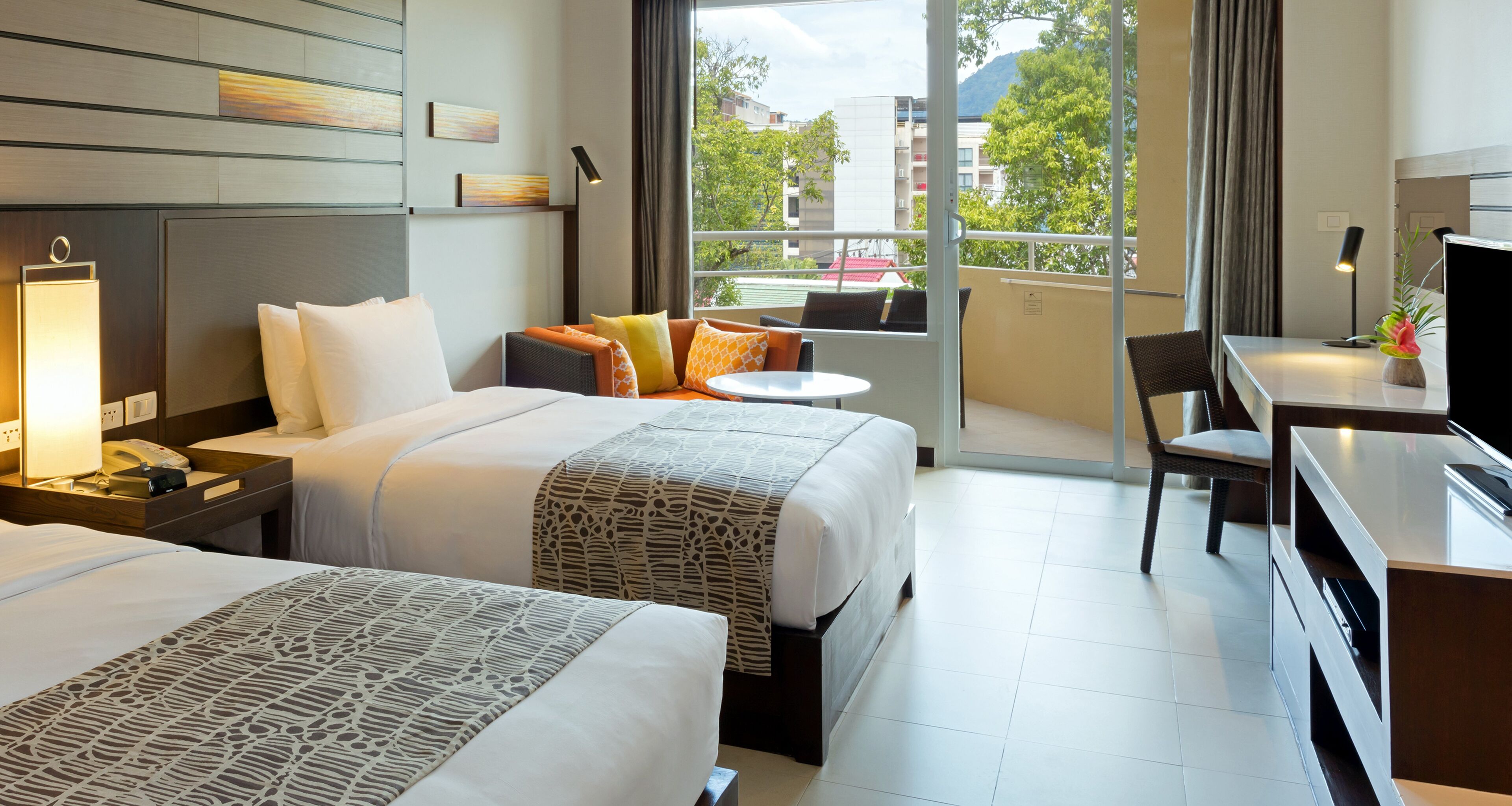 A hotel room with two beds, a desk, a chair, a balcony with a view, and a TV.