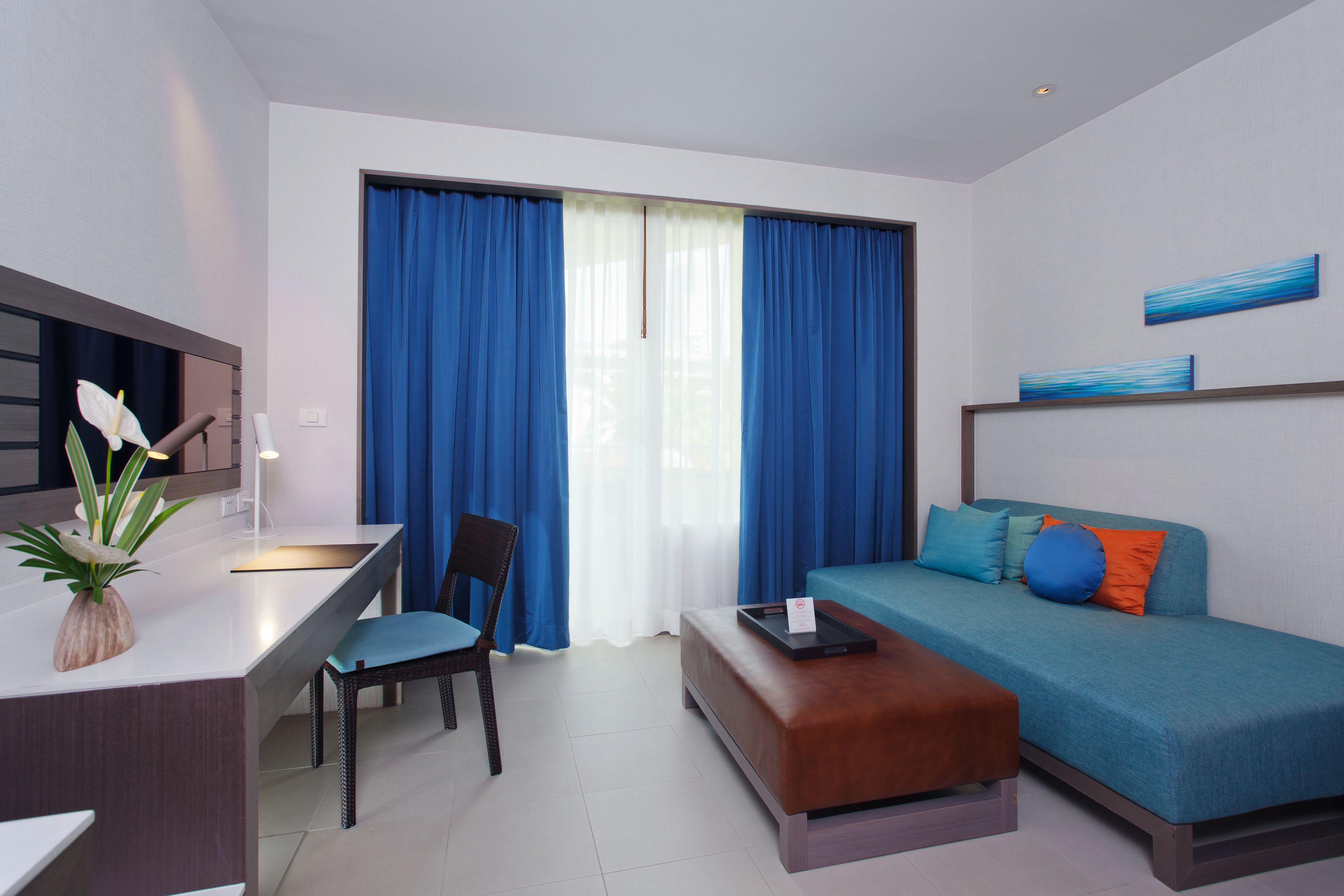 Una habitación de hotel moderna con sofá, zona de comedor y un gran ventanal con cortinas.