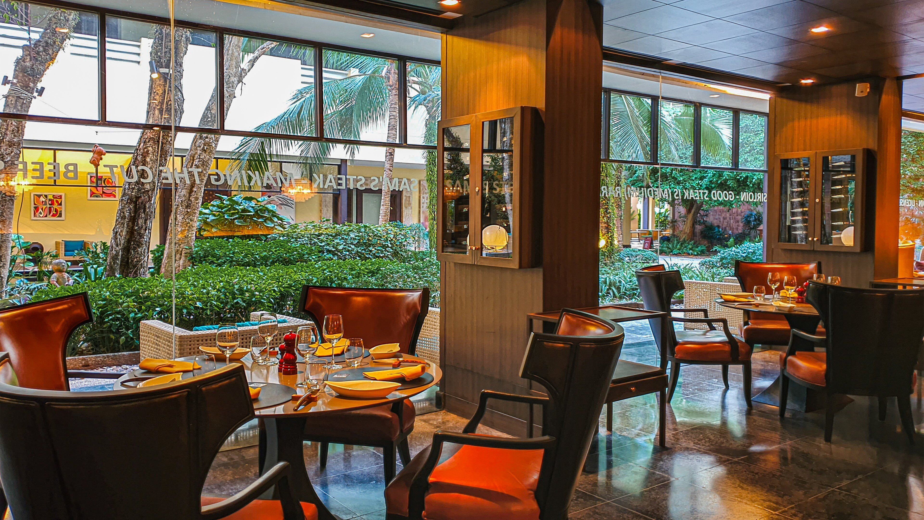 An indoor dining area with tables and chairs, large windows, and a view of greenery outside.