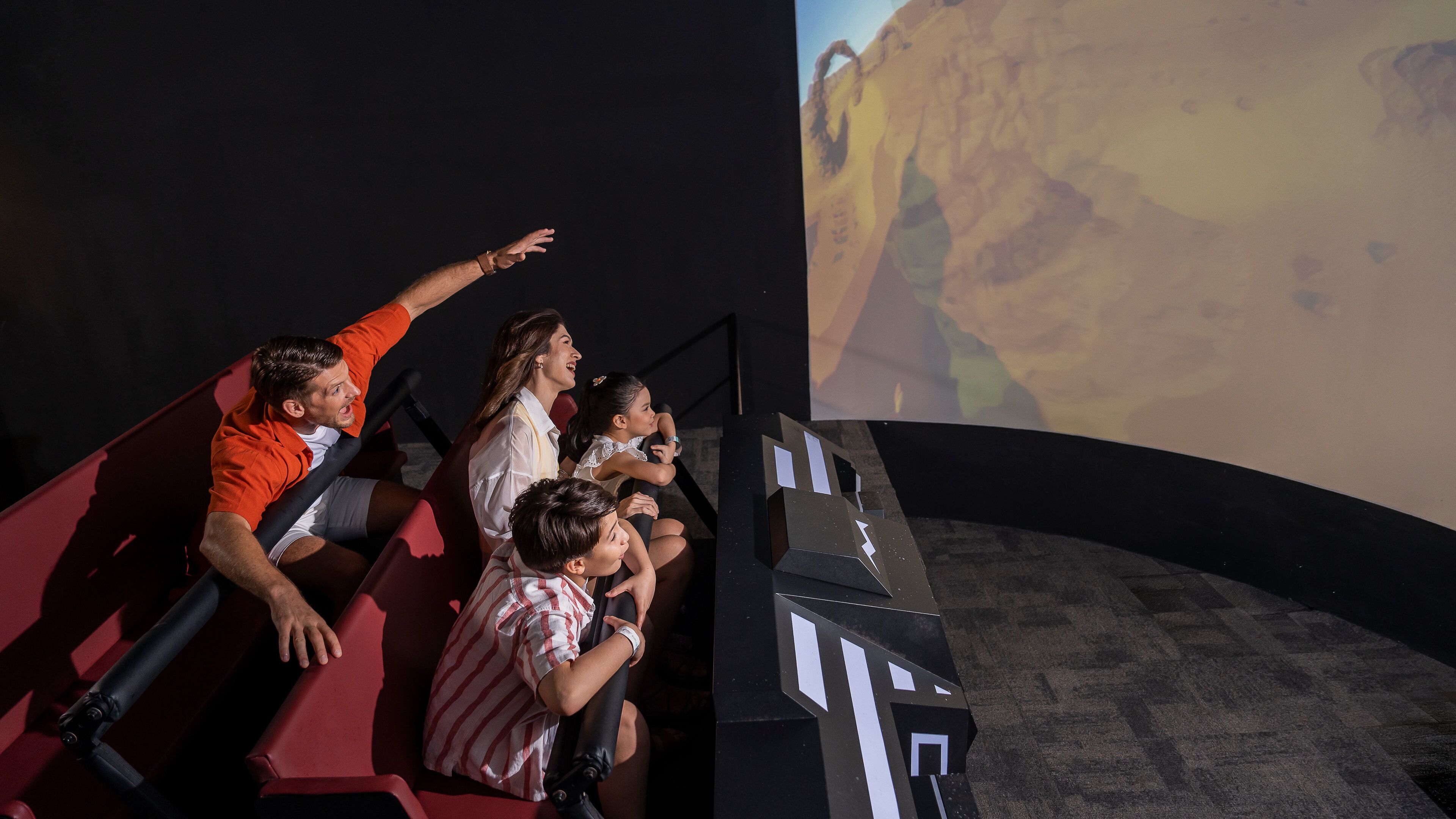 Un grupo de personas sentadas en un teatro con una pantalla grande que muestra un paisaje desértico.