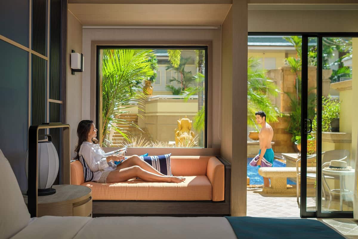 A modern hotel room with a large window, a sofa, and a bed.