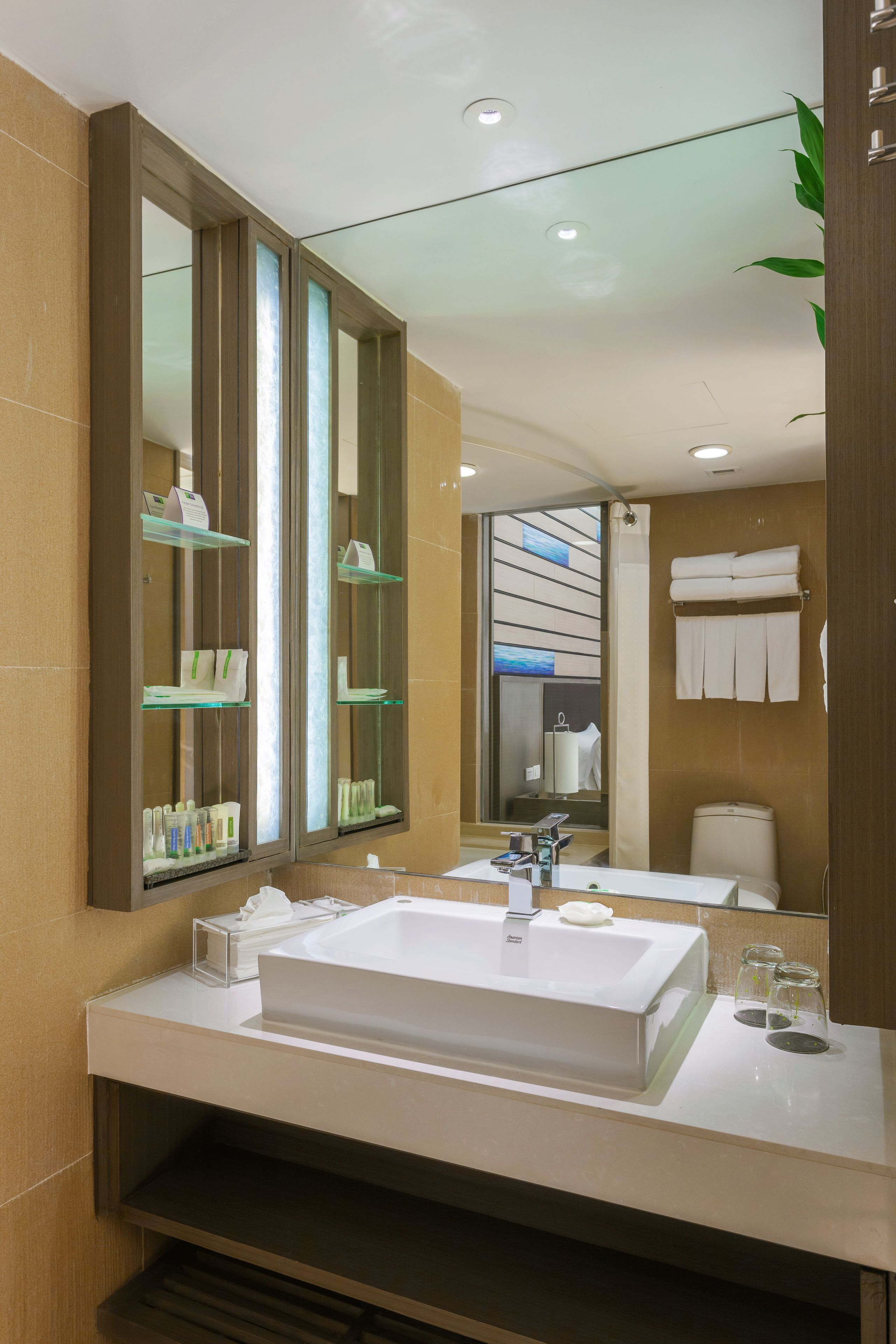 A modern bathroom with a large mirror, a white sink, and glass shelves.