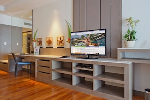 A modern hotel room with a wooden desk, a flat-screen TV, and a potted plant.