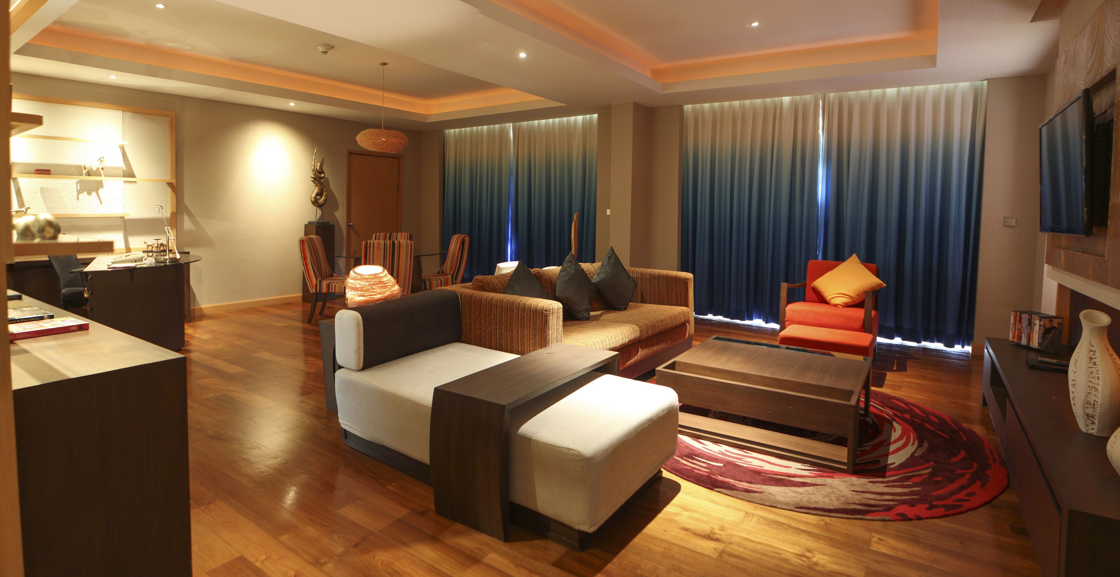 A modern living room with a sofa, ottoman, and coffee table, a television, and a desk with a lamp.