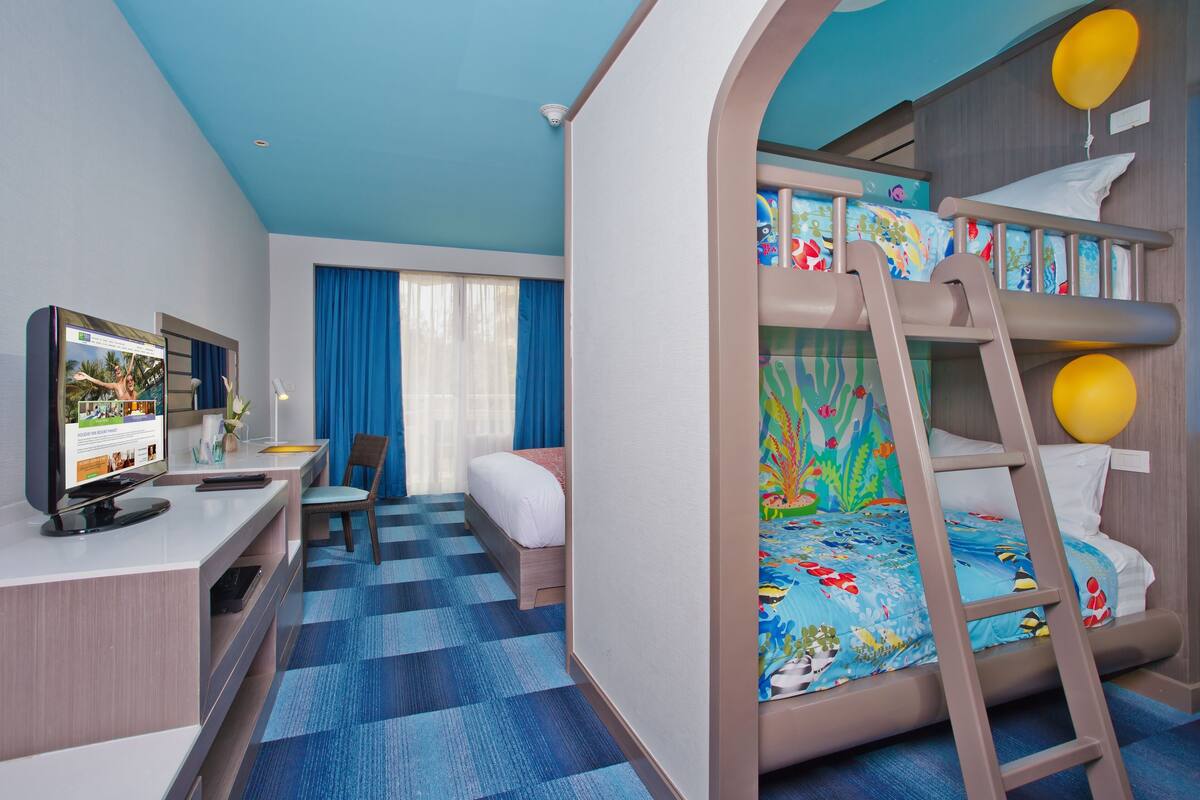 A hotel room with a bunk bed, a desk with a computer, a chair, and a television.