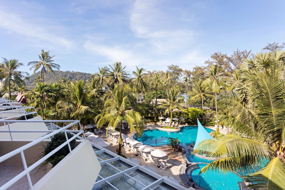 A resort with a pool surrounded by palm trees, lounge chairs, and a clear view of the mountains.