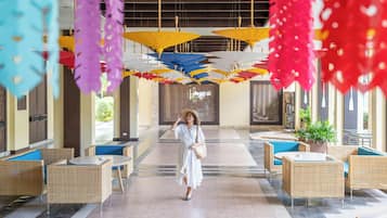 Un hall d'hôtel meublé de mobilier en osier, avec une allée centrale et des parasols colorés au-dessus.